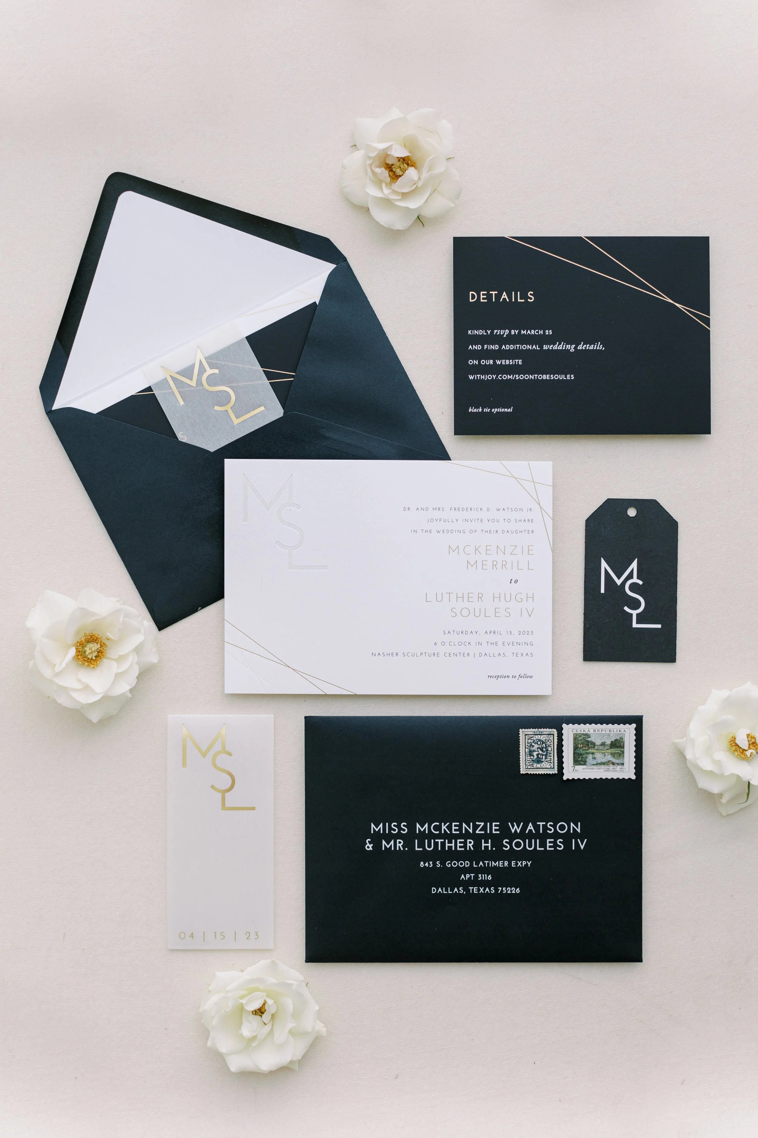 Elegant wedding invitation suite with black and white cards, floral accents, and postage stamps, arranged on a neutral background.