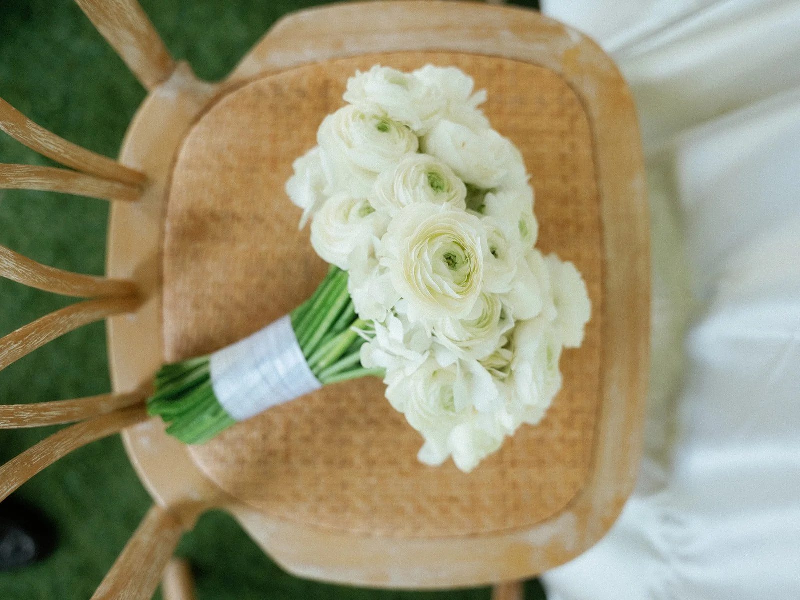 A bouquet of white flowers resting on a wooden chair with a woven seat.