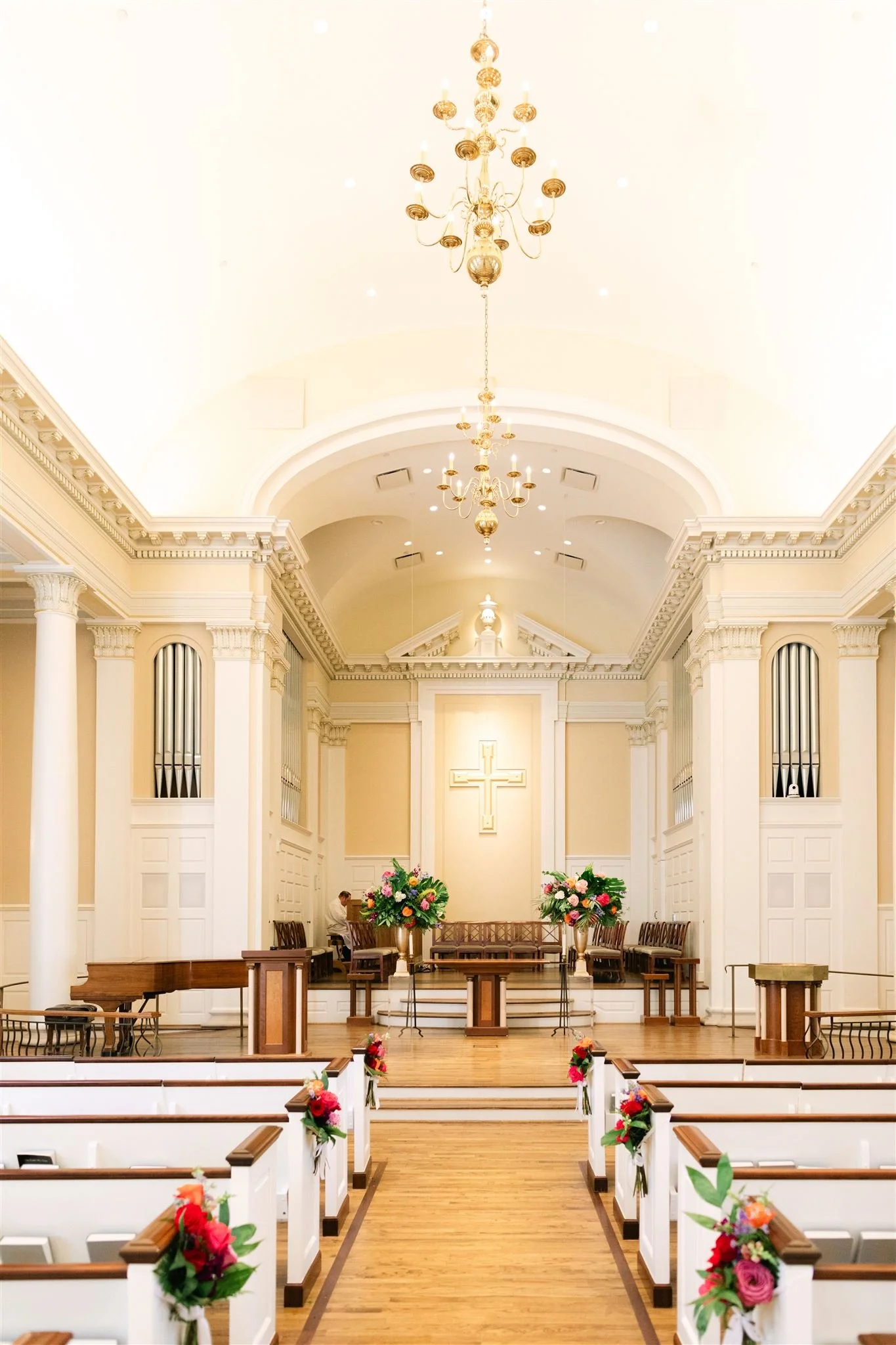 Interior of a church decorated for a wedding, with flowers on the pews and a cross at the front.