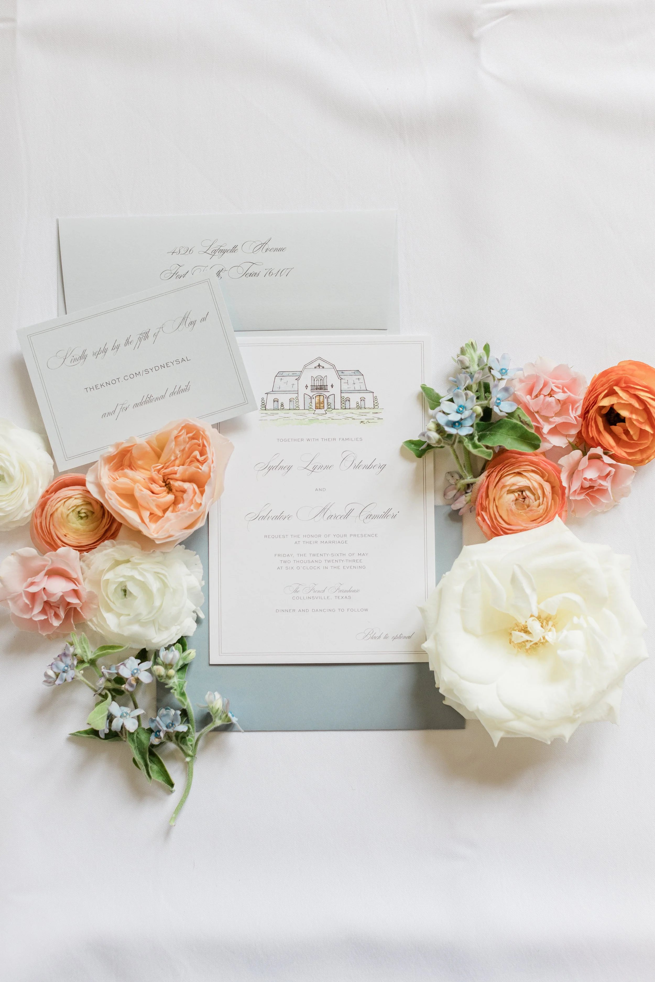 Wedding invitation with surrounding flowers, including roses and hydrangeas, on a white tablecloth.