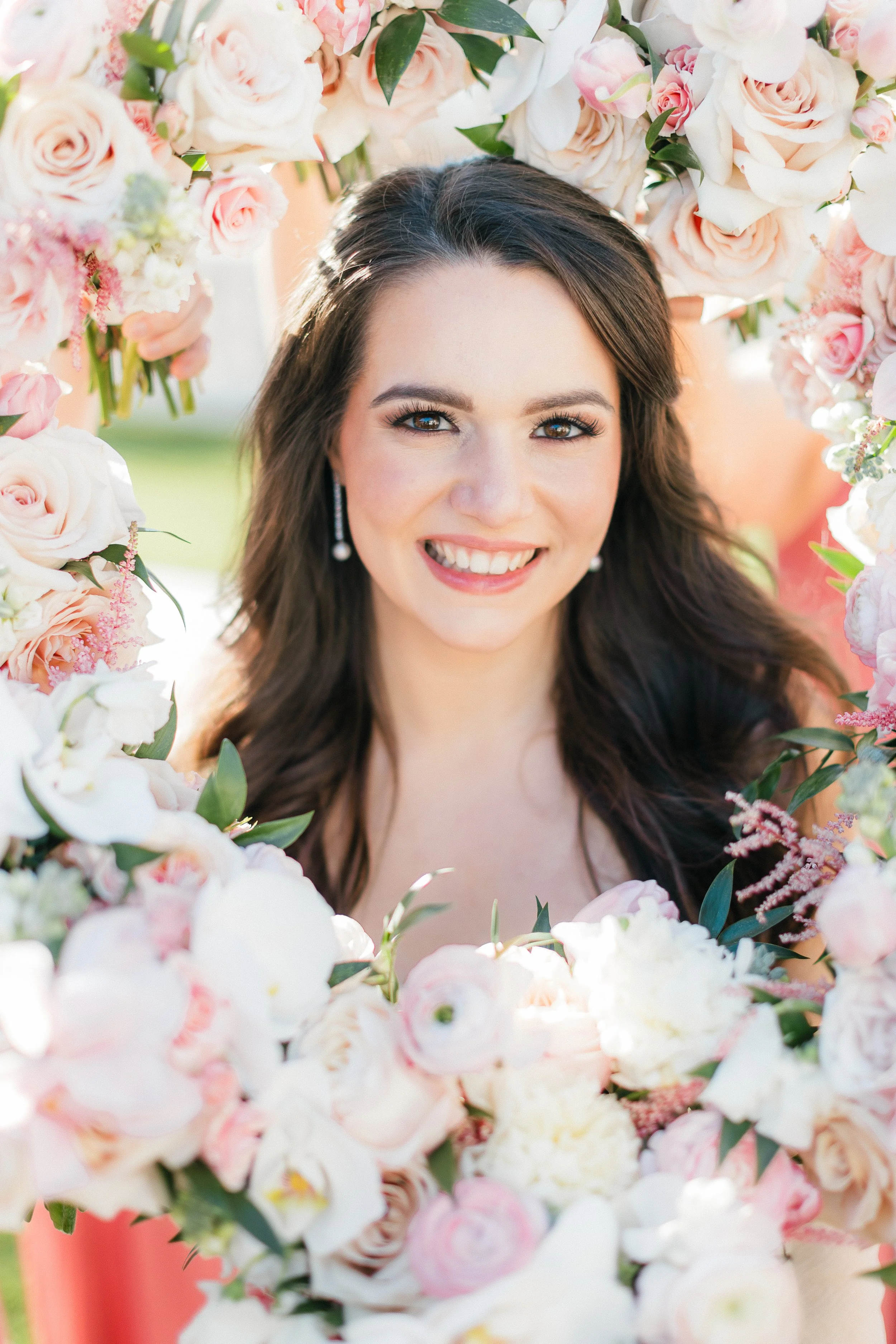 A woman smiling and looking at the camera surrounded by a large arrangement of pink and white flowers.