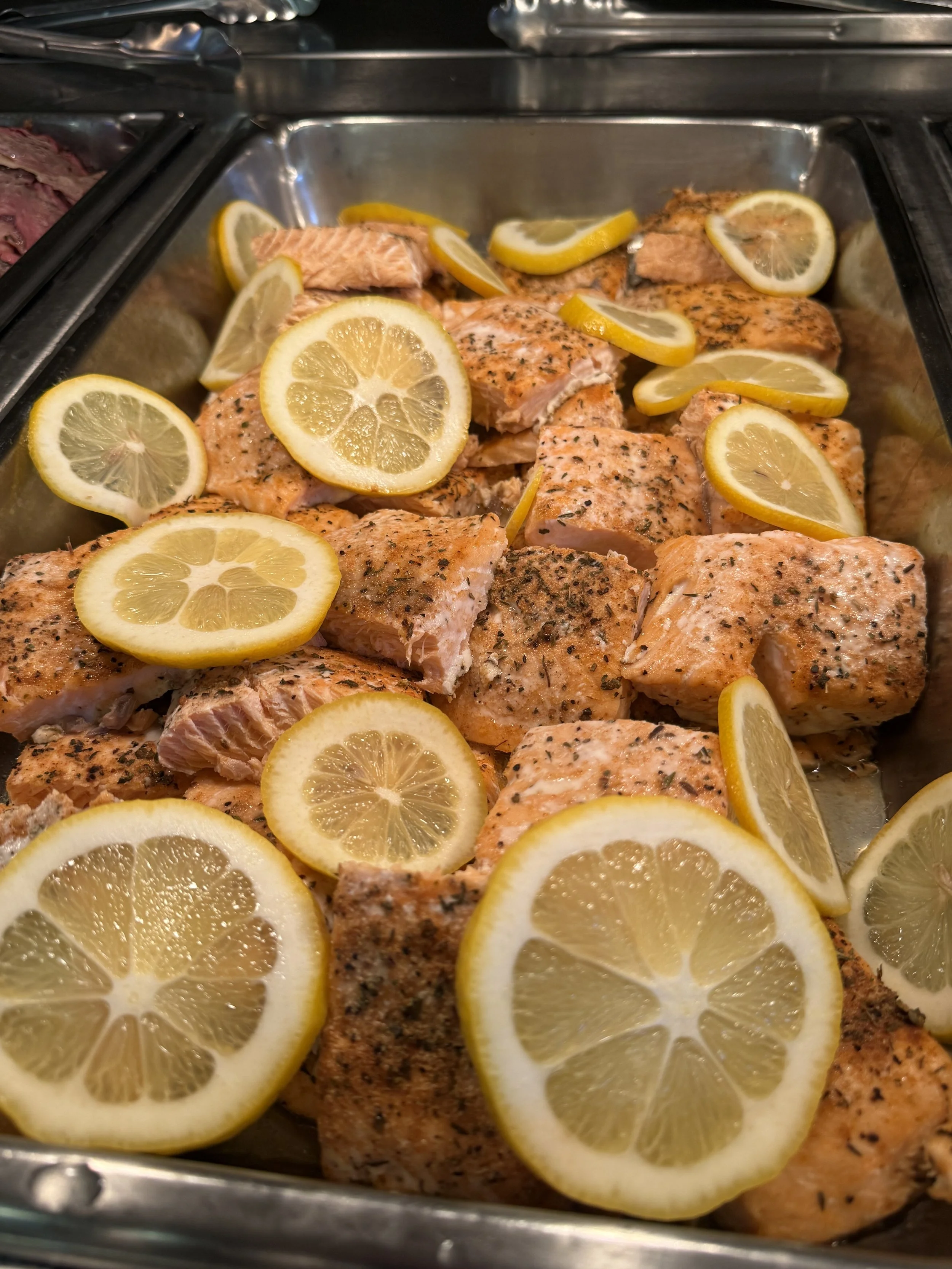 Chopped seasoned salmon fillets topped with lemon slices in a metal serving pan.