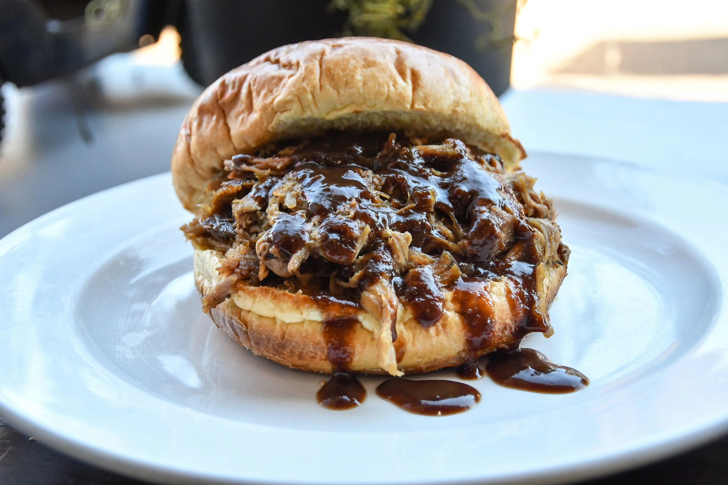 Pulled pork sandwich with barbecue sauce on a bun served on a white plate.