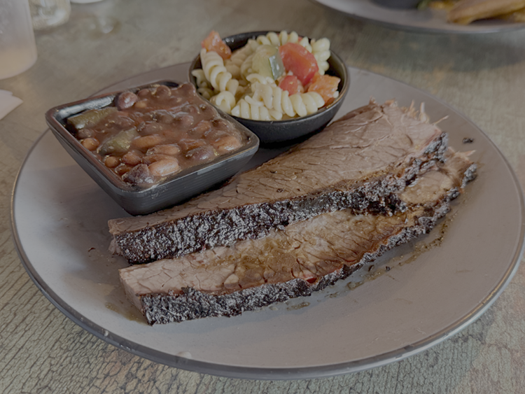 A plate with two slices of cooked brisket, baked beans, and macaroni salad in a small bowl.