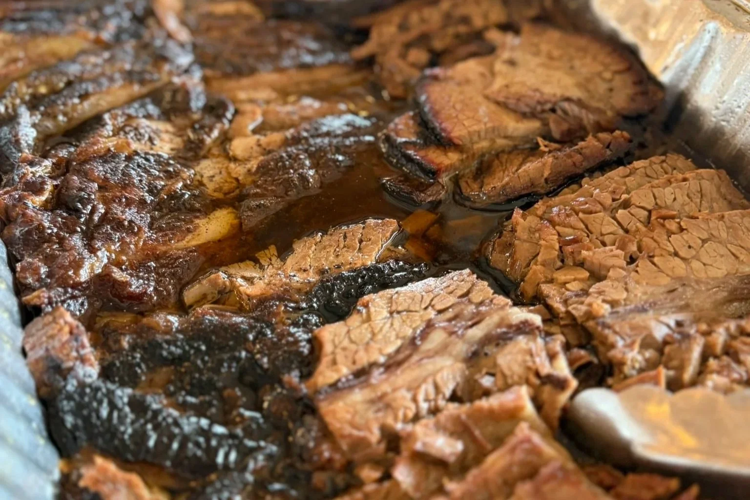 Close-up of cooked barbecue meats including ribs, brisket, and sausage.