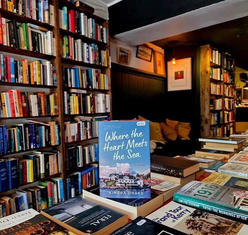 A paperback copy of Where The Heart Meets The Sea stands on a table of books inside a bookstore