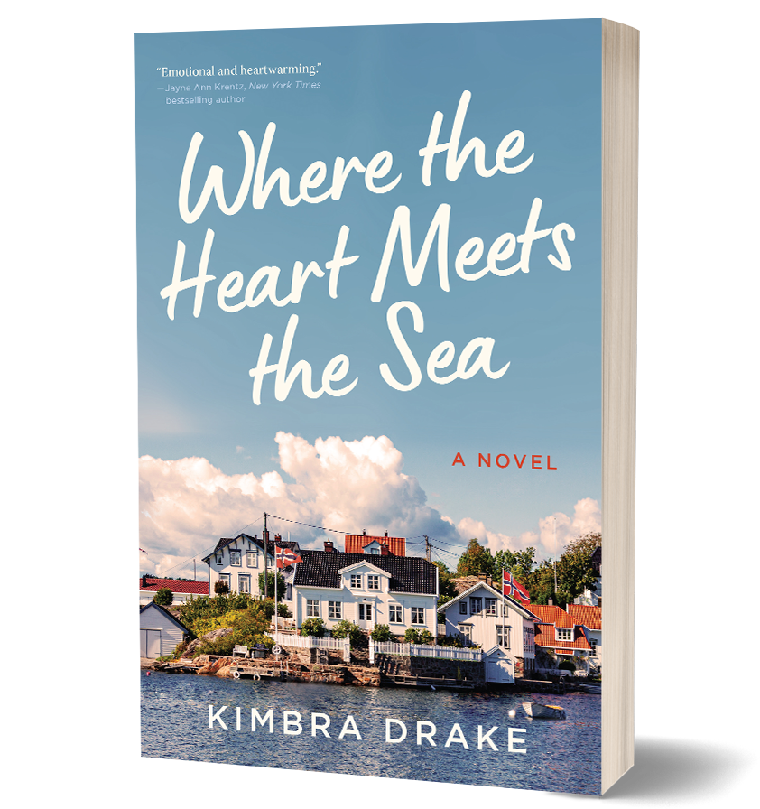 A book cover featuring a group of houses by the water, with a cloudy sky above. The title "Where the Heart Meets the Sea" is prominently displayed along with the author's name, Kimbra Drake, and a quote praising the book.