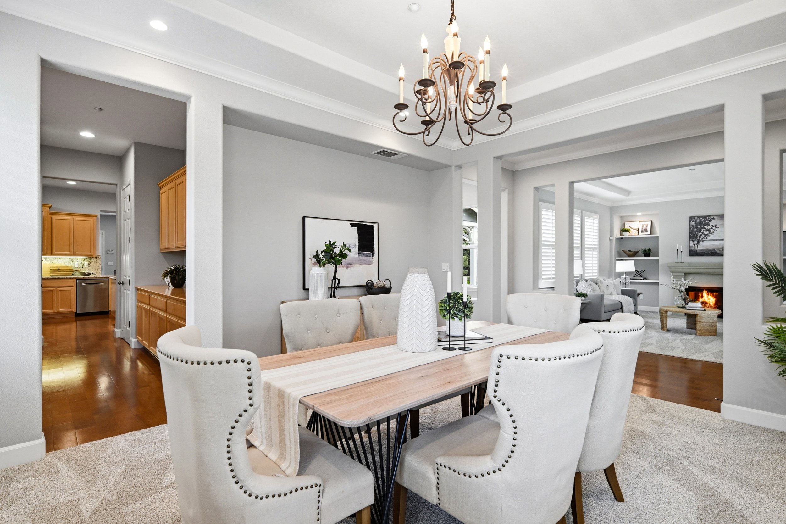 Open-concept living and dining area with white walls, wooden floors, chandelier, and furniture including a dining table with chairs and a cozy sitting area with a fireplace.