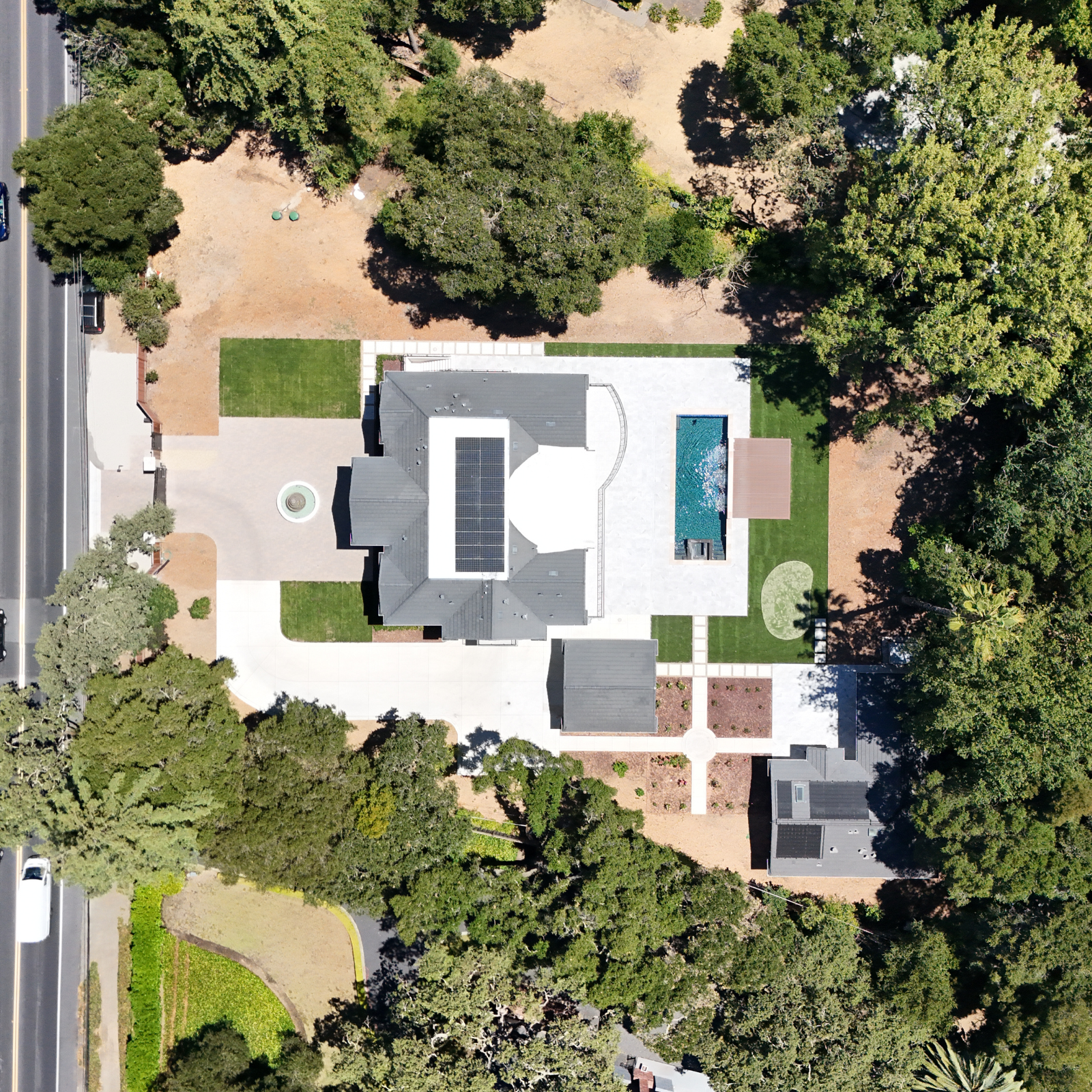 An aerial view of a modern house with a backyard swimming pool, surrounded by lush greenery and trees.