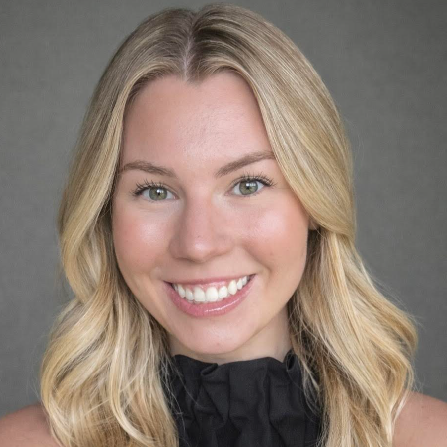 A young woman with blonde, wavy hair and green eyes smiling against a gray background.