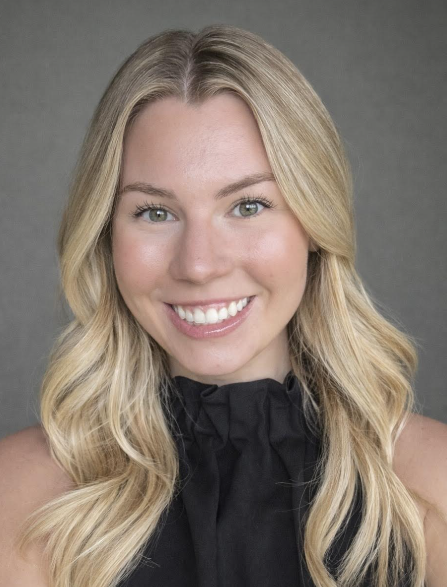 Headshot of a smiling woman with long blonde hair, green eyes, and a black ruffled top, against a gray background.