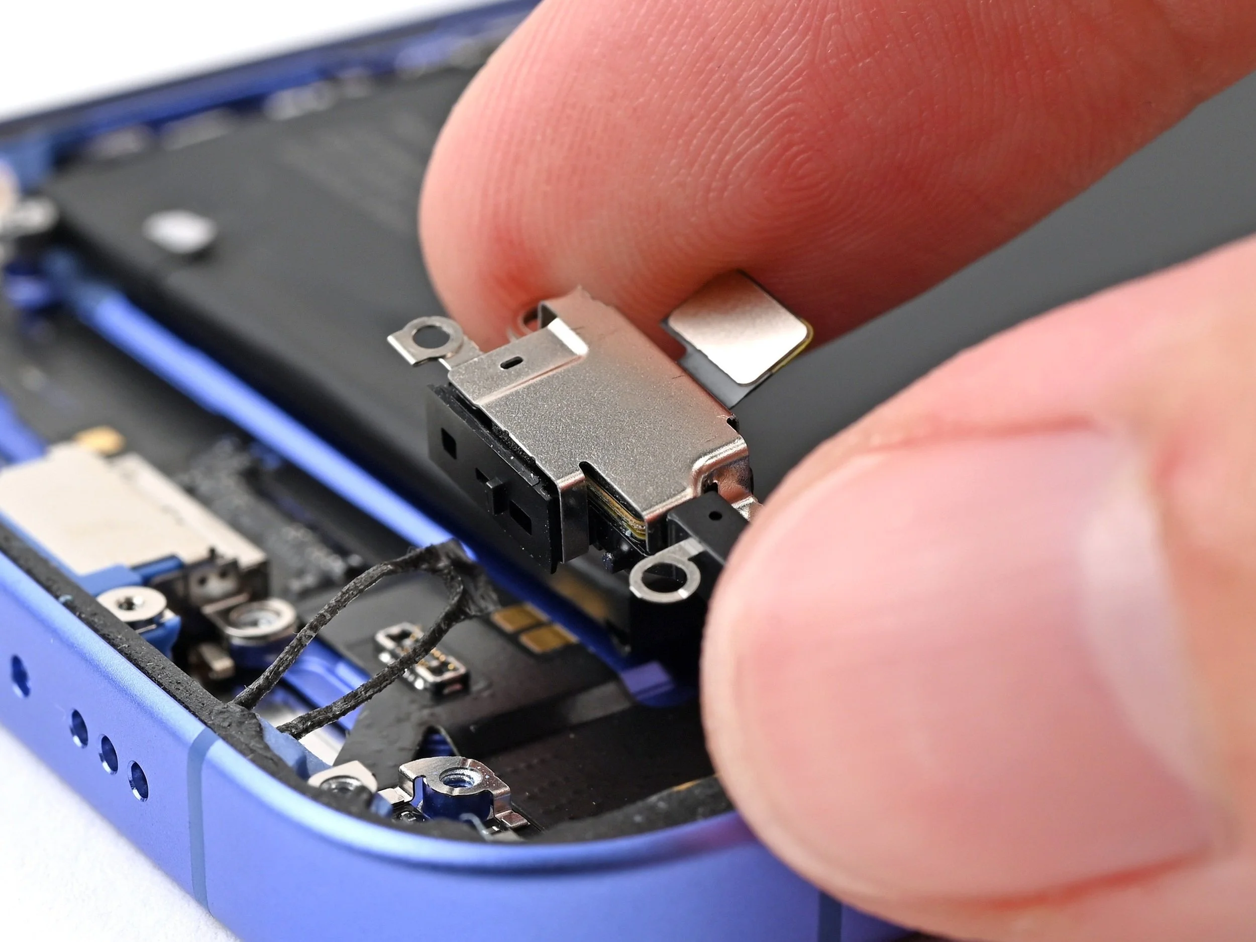 Close-up of a person's finger pressing down on a computer component inside a device, with visible electronic parts and a blue case.
