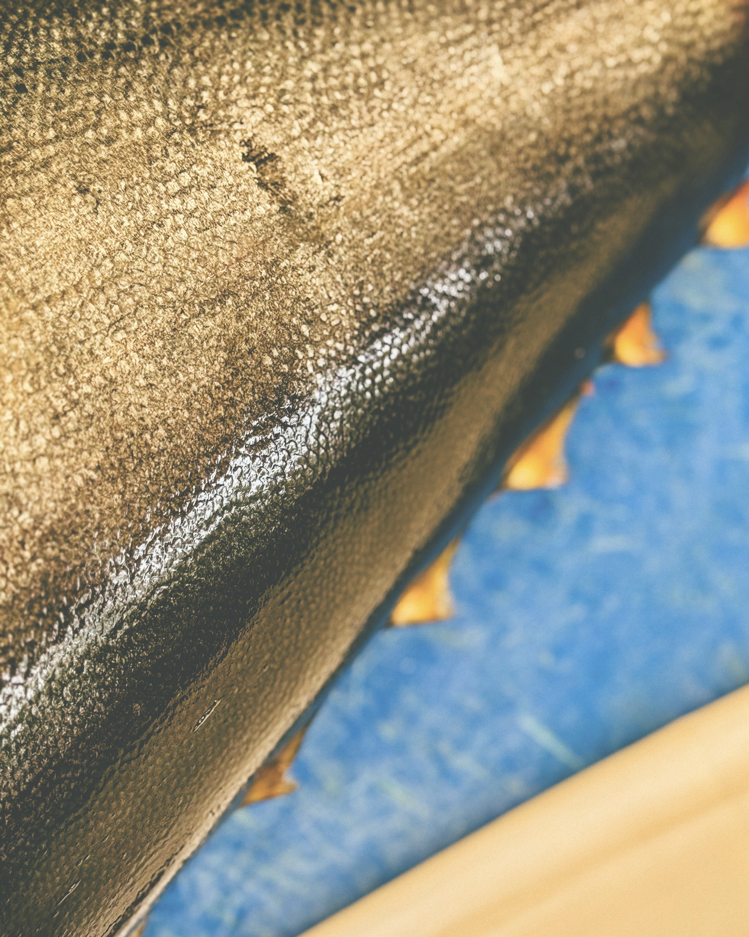 Primer plano de la superficie de un objeto negro con textura y brillo, rodeado de hojas secas amarillas y fondo azul.