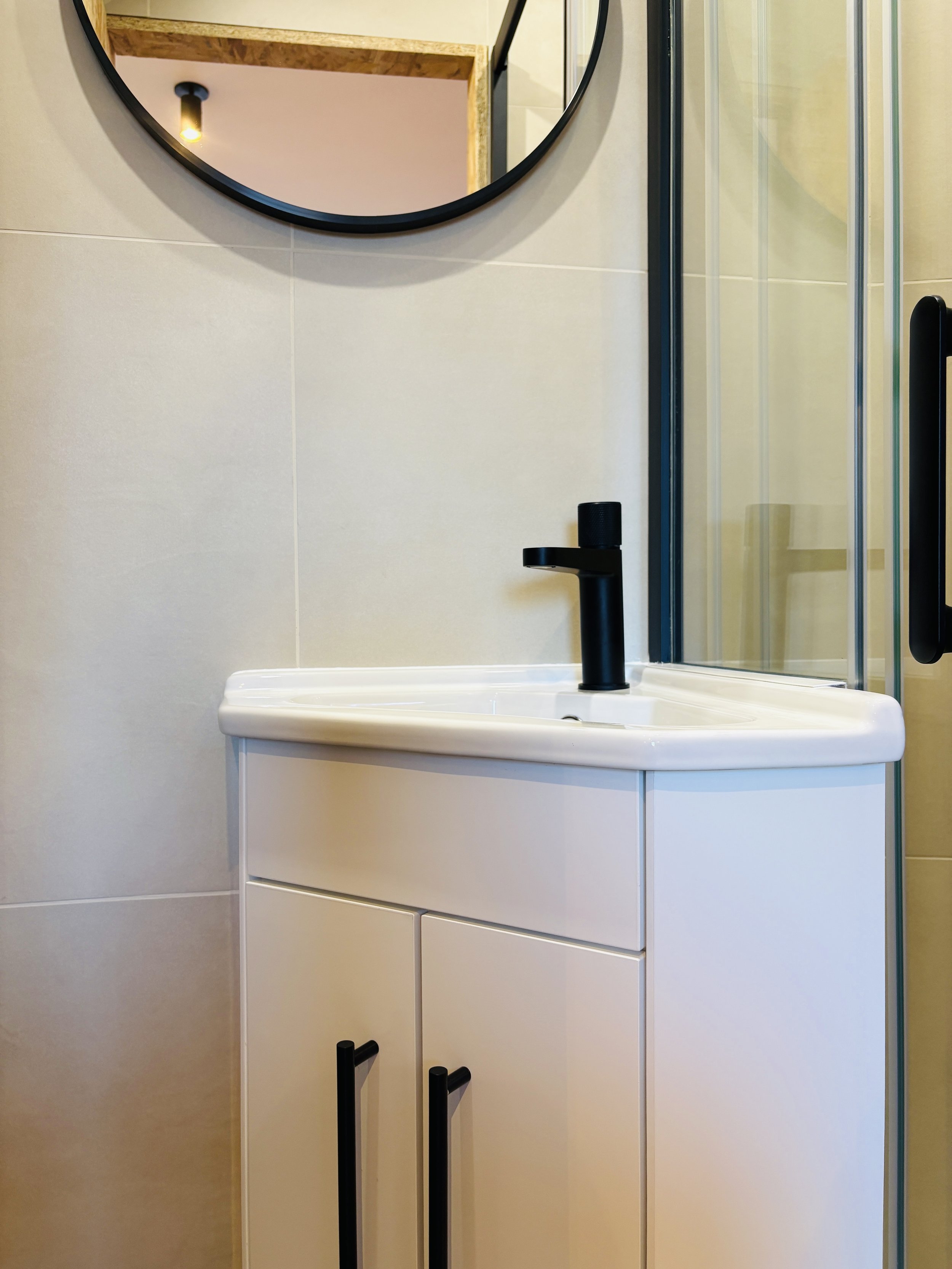 Un lavabo blanc avec un robinet noir dans une salle de bain moderne. Un miroir rond est accroché au mur au-dessus du lavabo.