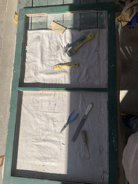 One of a set of a dozen original storm windows in need of restoration. Old brittle glazing is softened with an infrared heat lamp, and scraped clean from the glazing bed, and the original glass panes.
