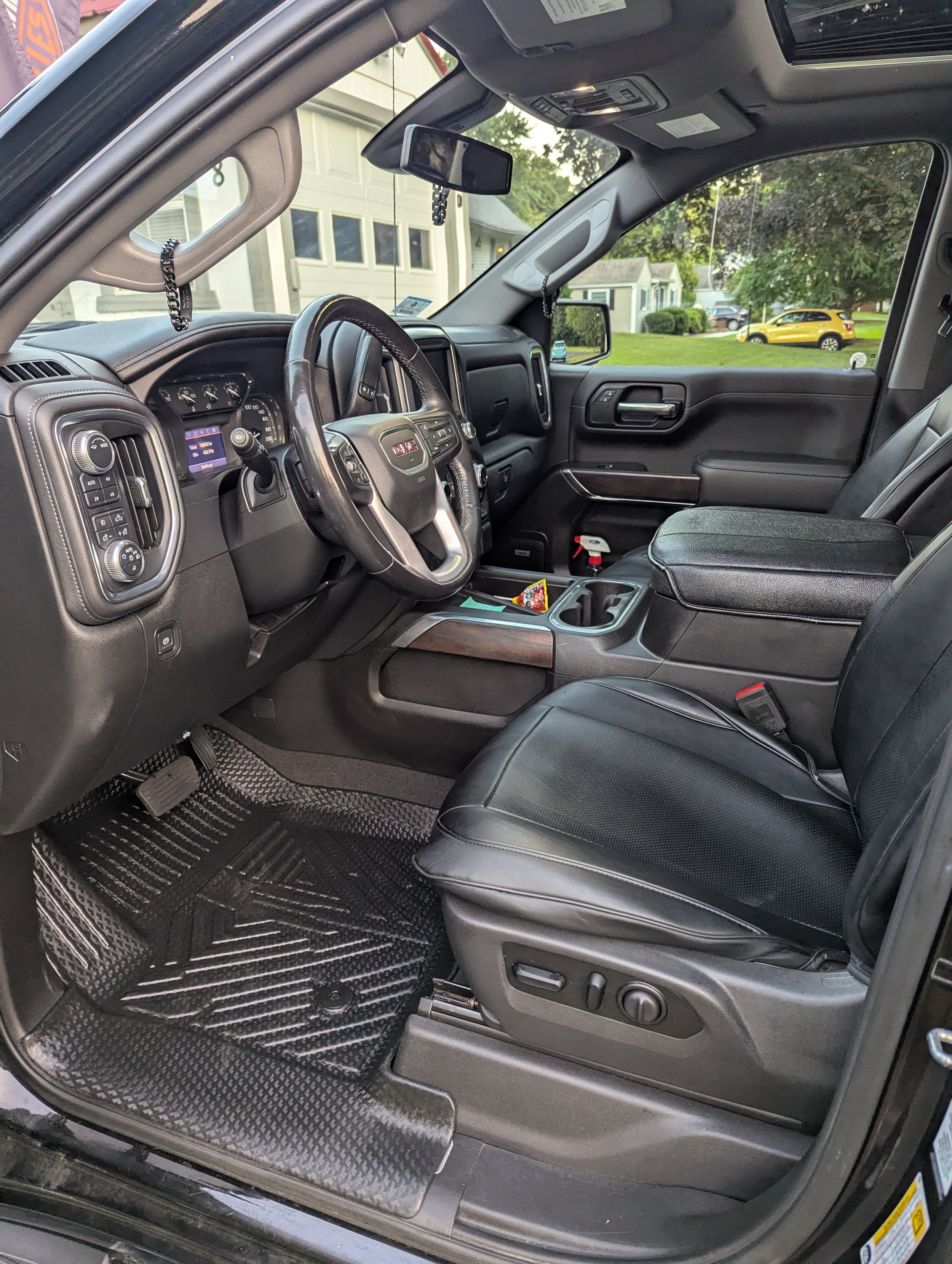 Interior view of a black GMC truck's driver's side with a leather seat, dashboard, steering wheel, and center console, parked in a residential neighborhood.
