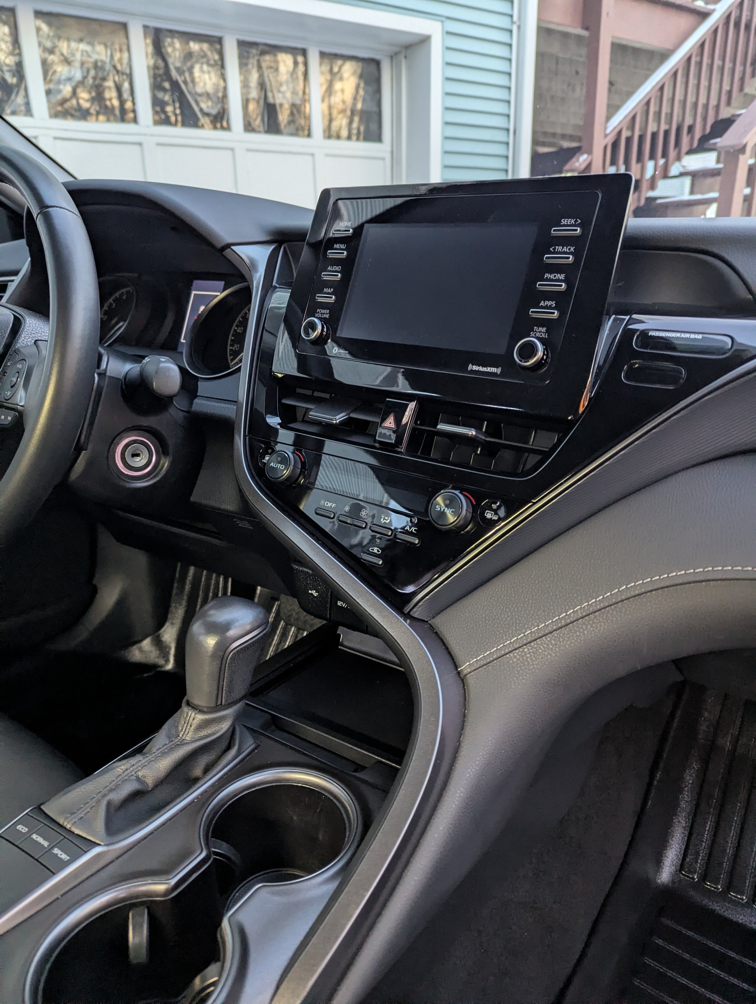Interior of a car dashboard showing a touchscreen display, climate control, gear shift, and cup holders.