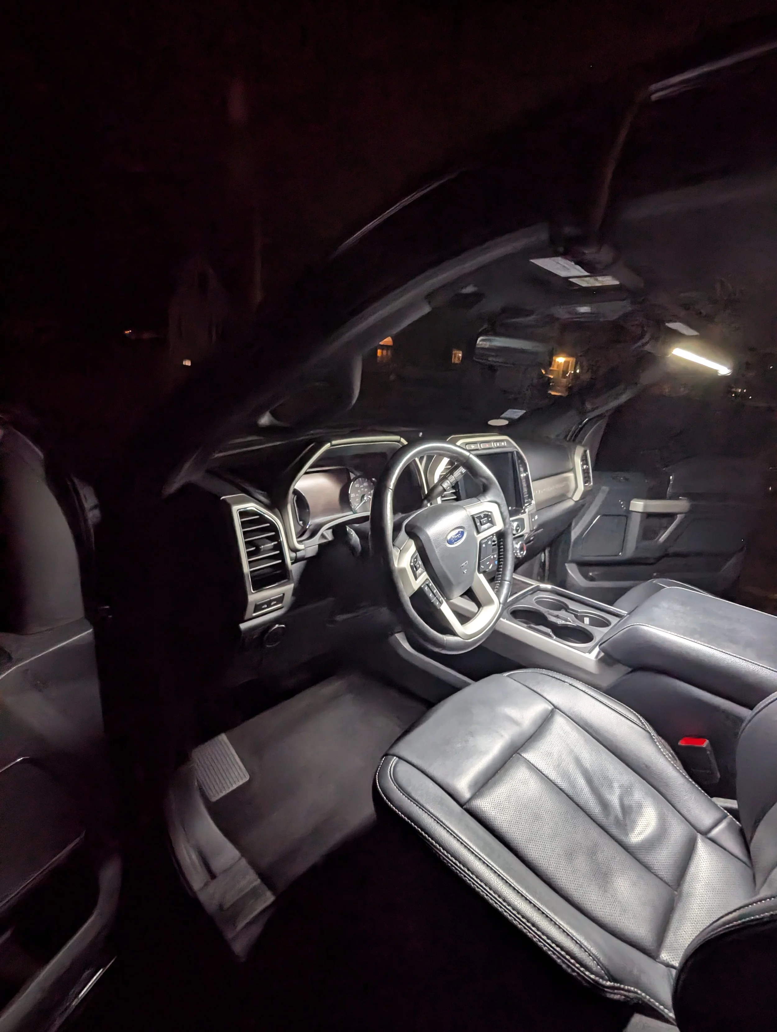 Interior of a vehicle at night, showing the dashboard, steering wheel, and front seats.