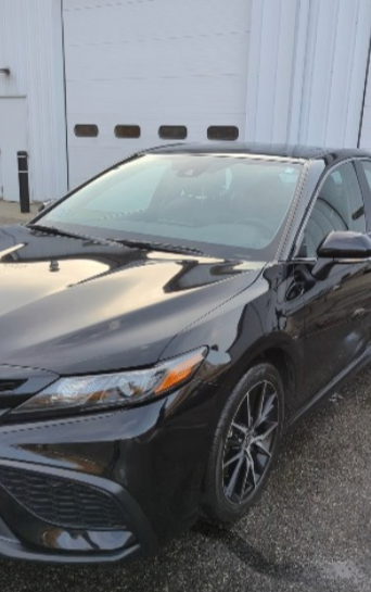 A black sedan parked outdoors in front of a light-colored garage door.