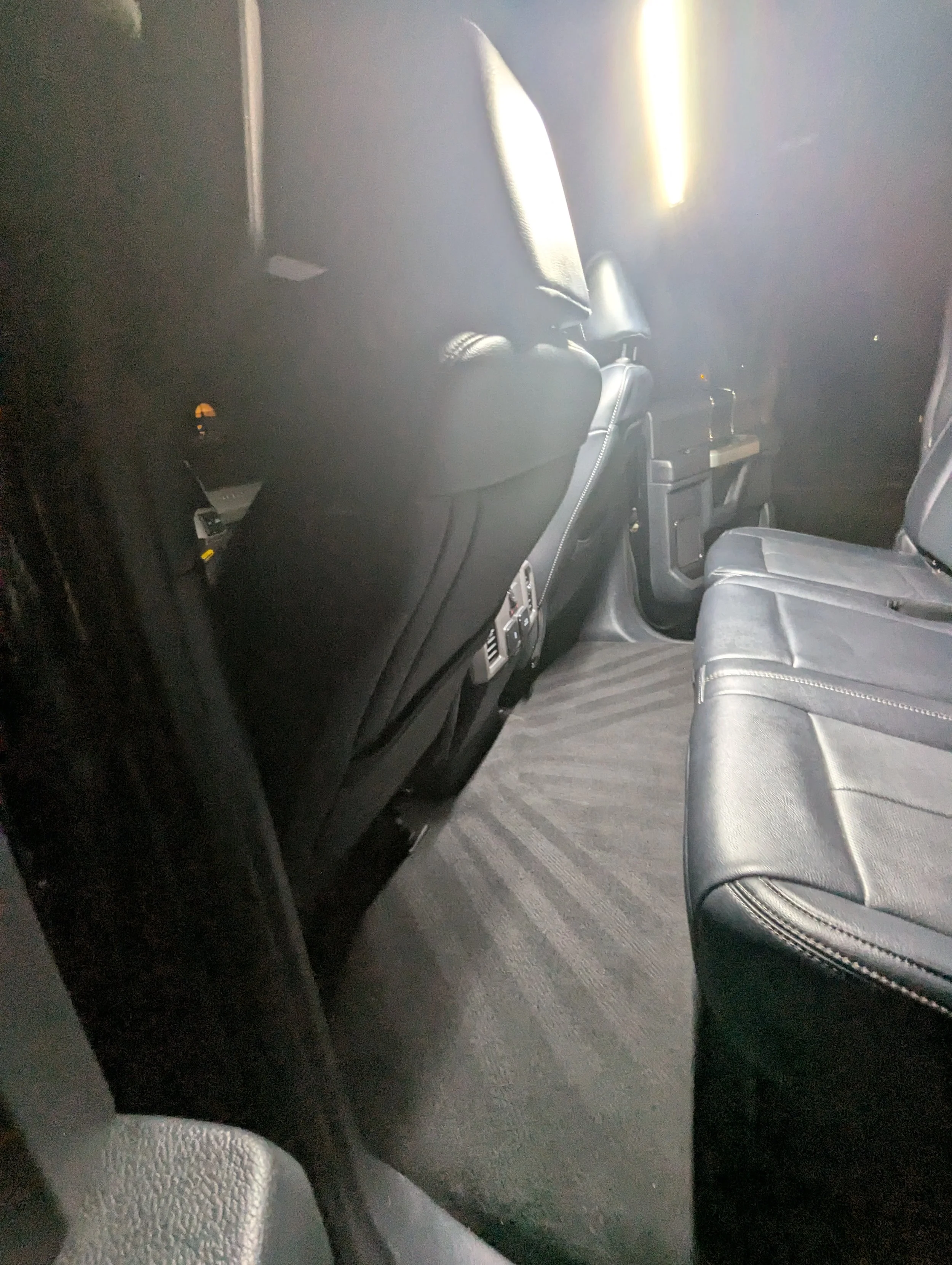 Inside of a vehicle showing the back of the front seats, the middle row of seats, and the floor with carpet and air vents.