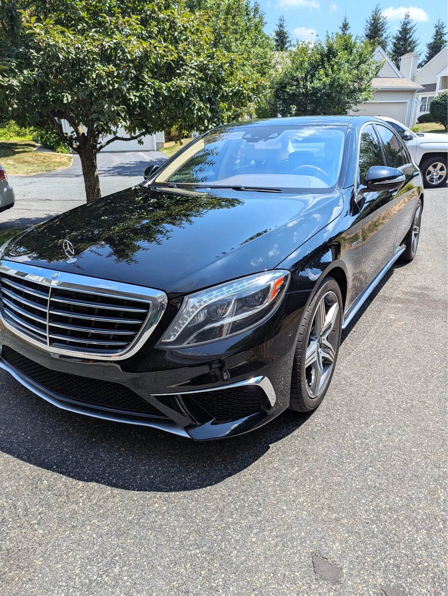 Black Mercedes-Benz sedan parked on a residential street with trees and houses in the background.