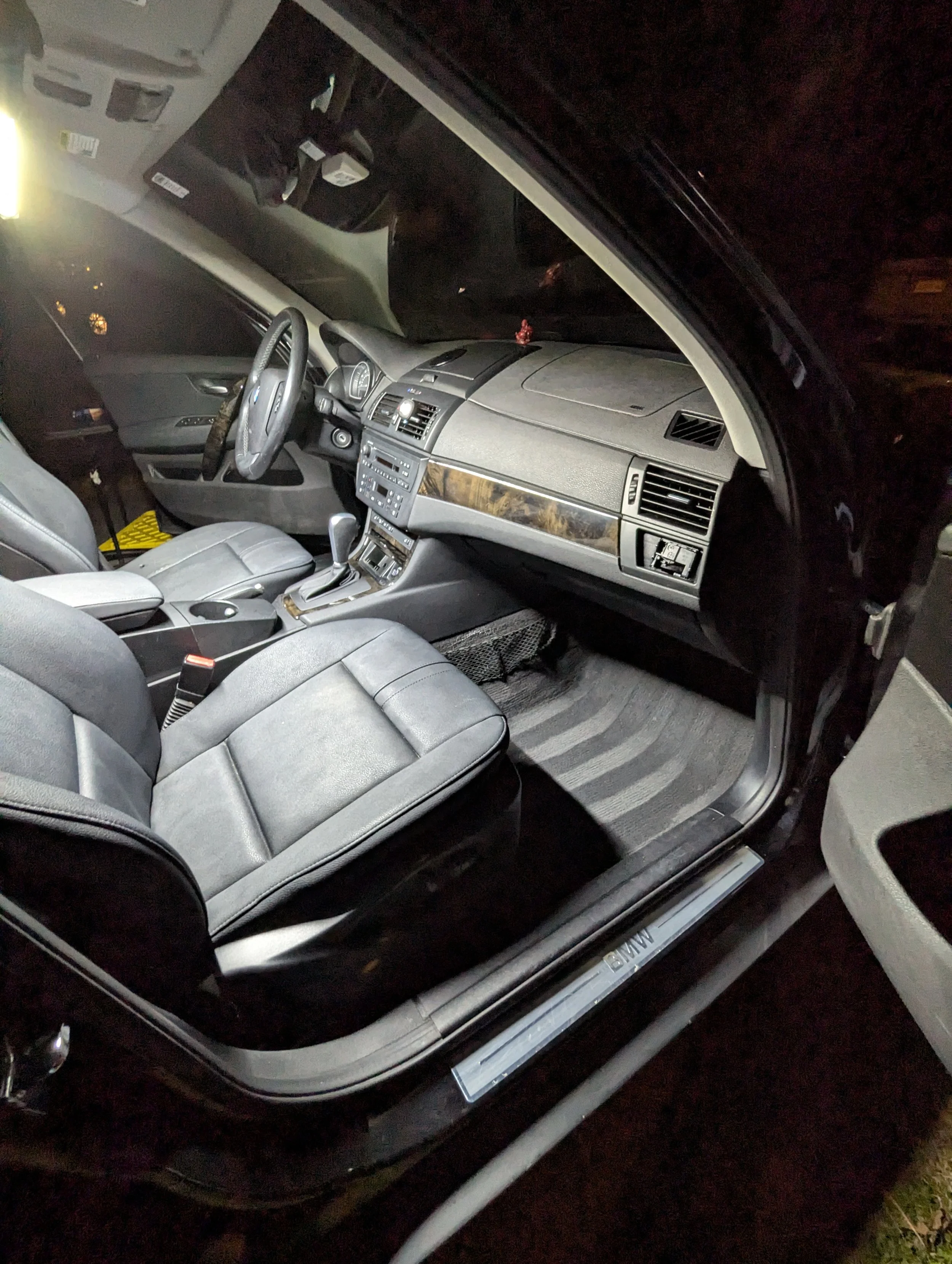 Interior of a black BMW car showing the front seats, dashboard, steering wheel, gear shift, and floor mats.