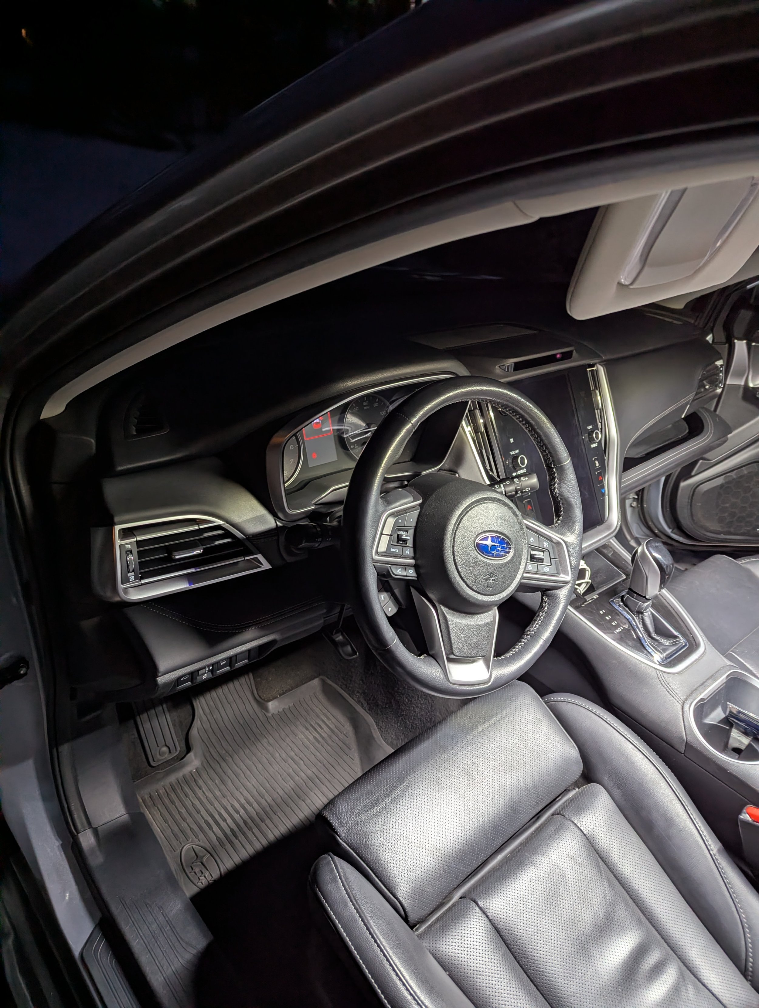 Interior of a black Subaru car showing the steering wheel, dashboard, gear shift, front seat, and floor mats.