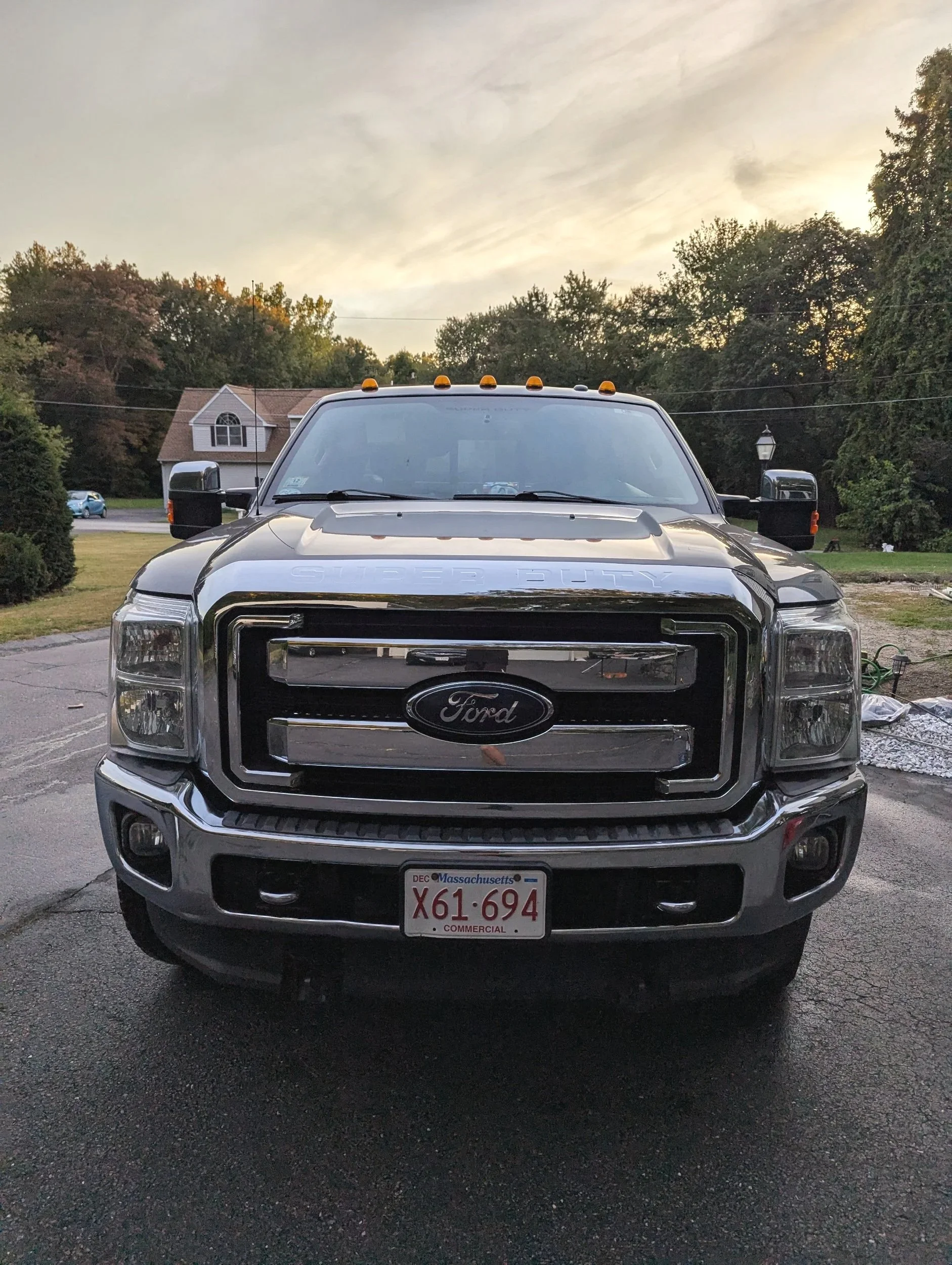 Front view of a black Ford Super Duty truck with Massachusetts license plate parked on pavement with trees and sky in the background.