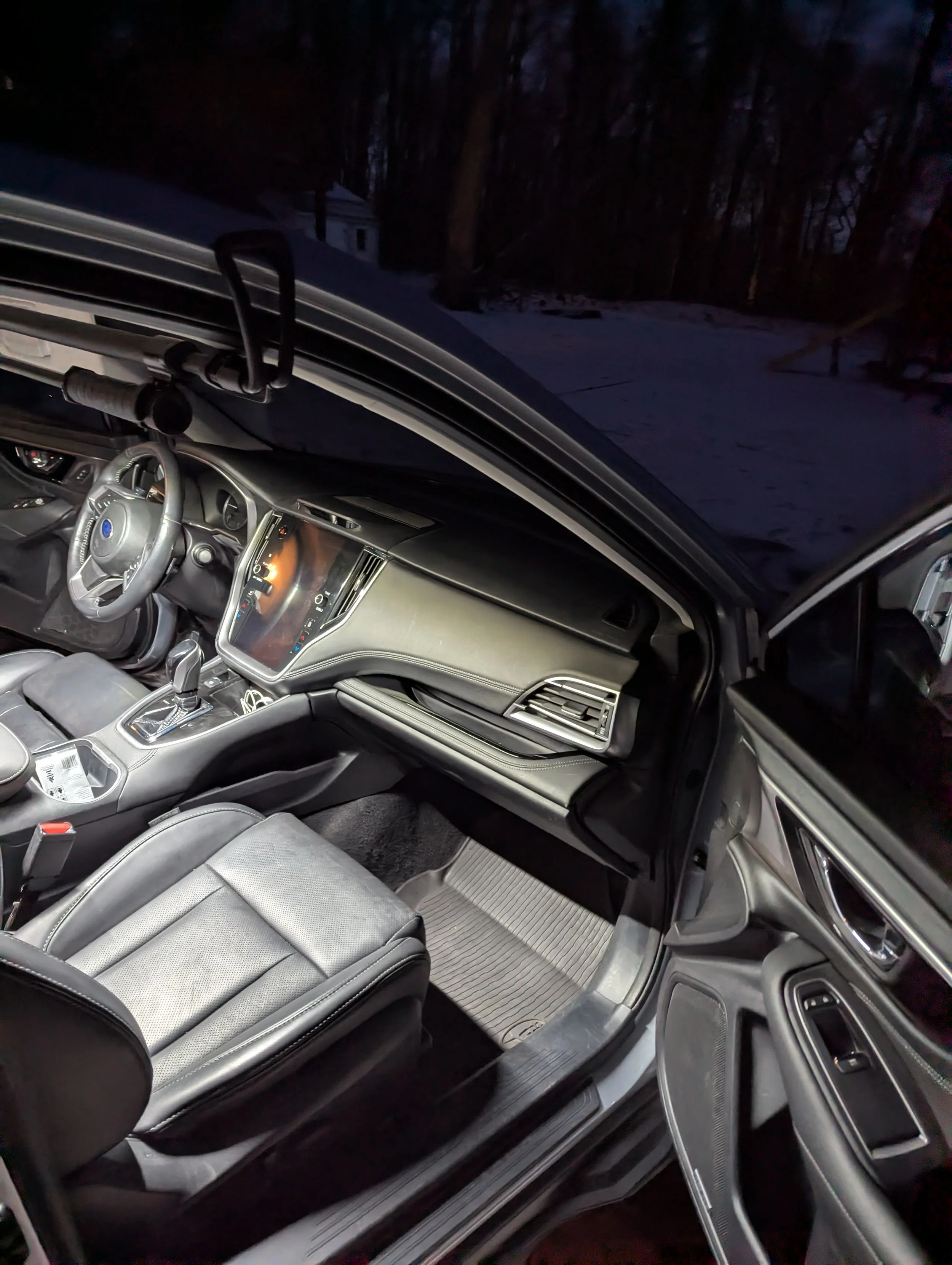 Interior of a modern car at night, showing the driver's seat, dashboard, center console, and part of the passenger seat, with a snowy landscape visible through the windshield.