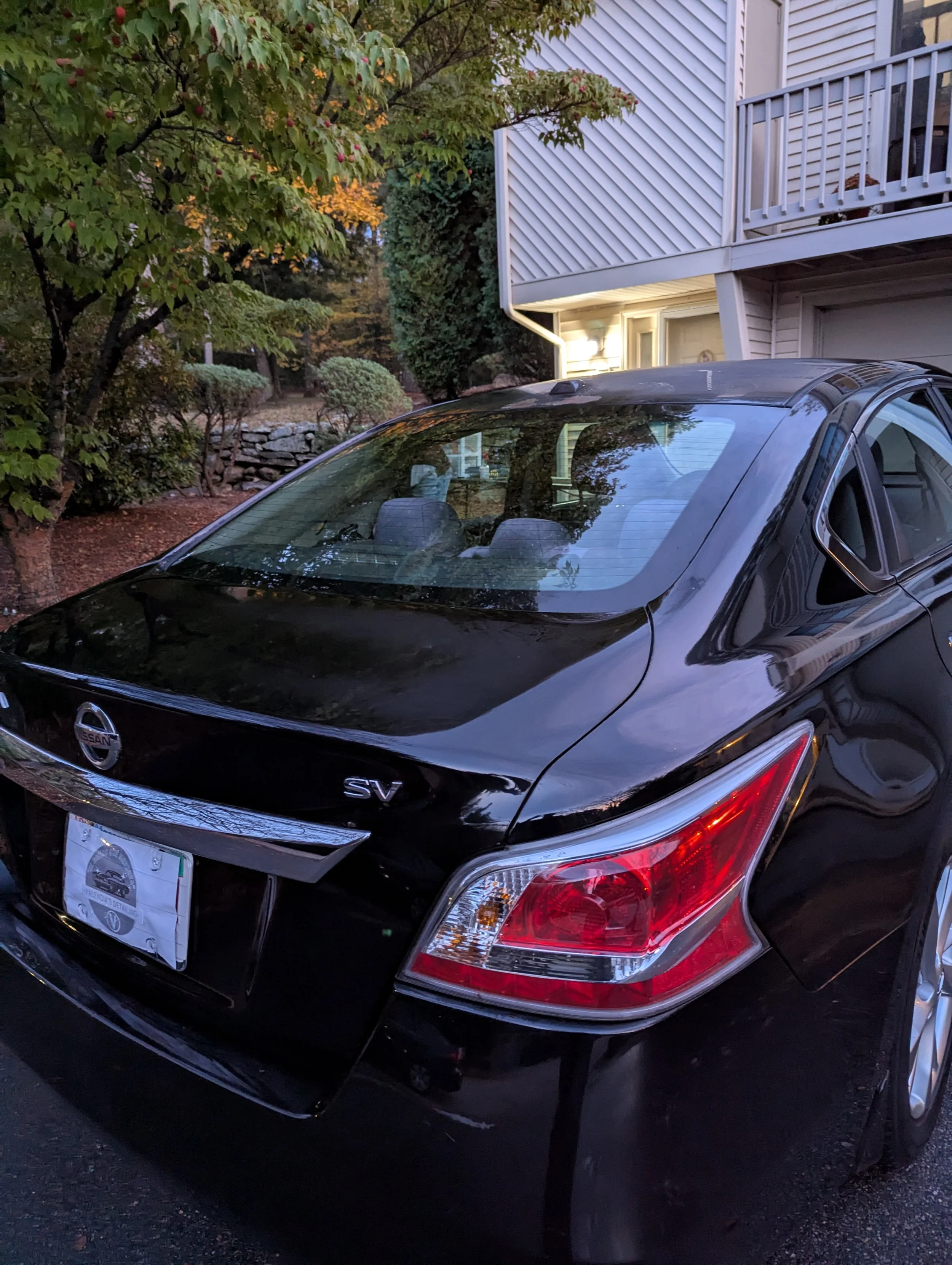 Black Nissan Sentra SV parked outdoors near a residential building with trees and bushes in the background.