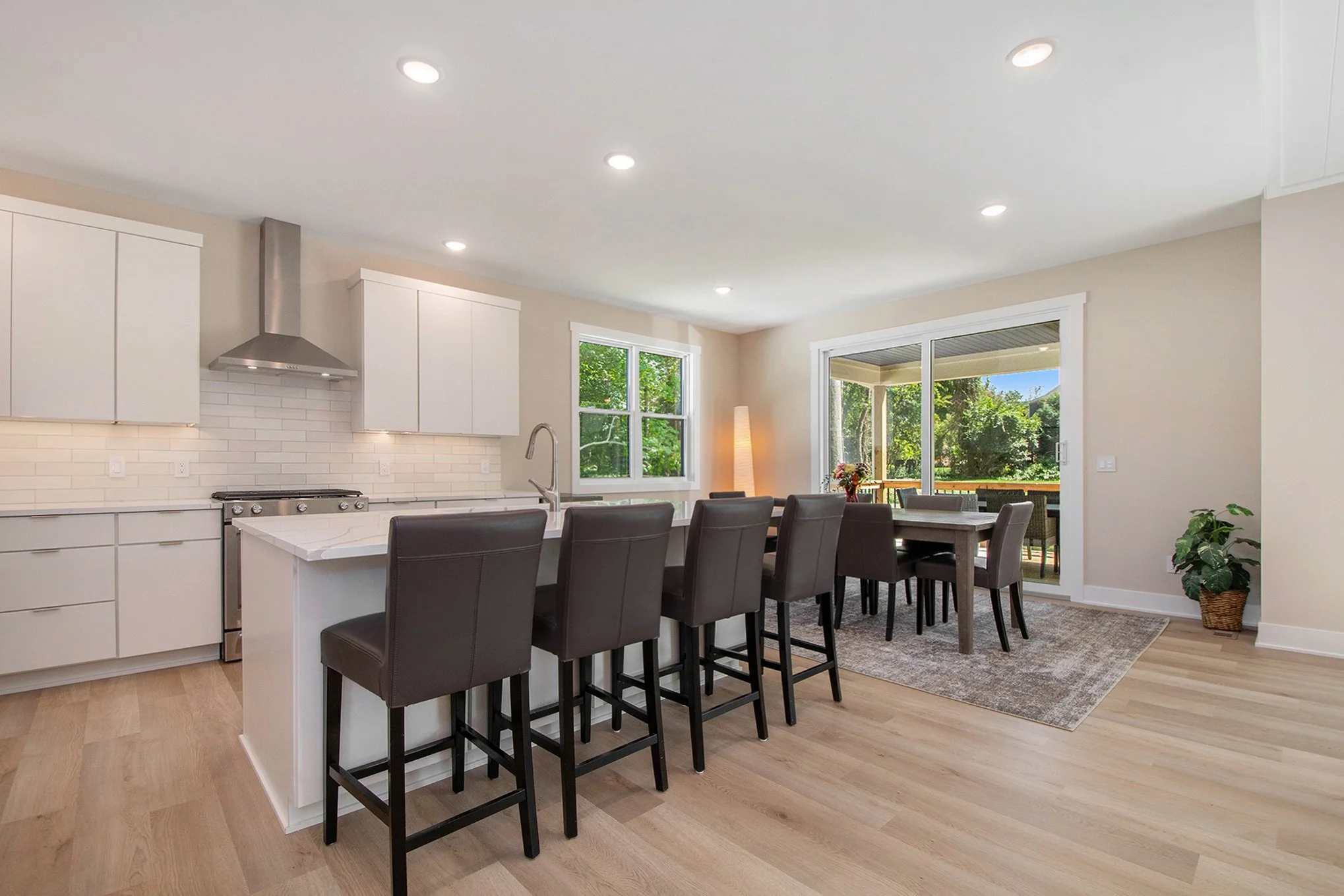Modern open-concept kitchen and dining area with white cabinets, a kitchen island, black bar stools, and a sliding glass door leading to an outdoor patio.
