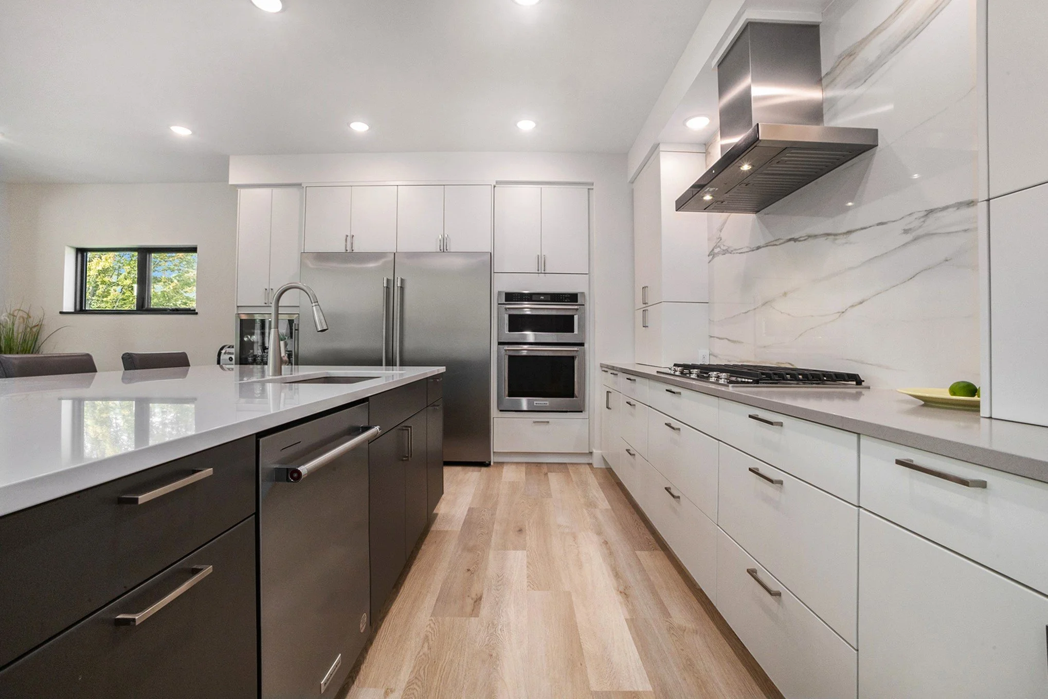 Modern kitchen with white cabinets, stainless steel appliances, wooden floor, and a large white countertop island.