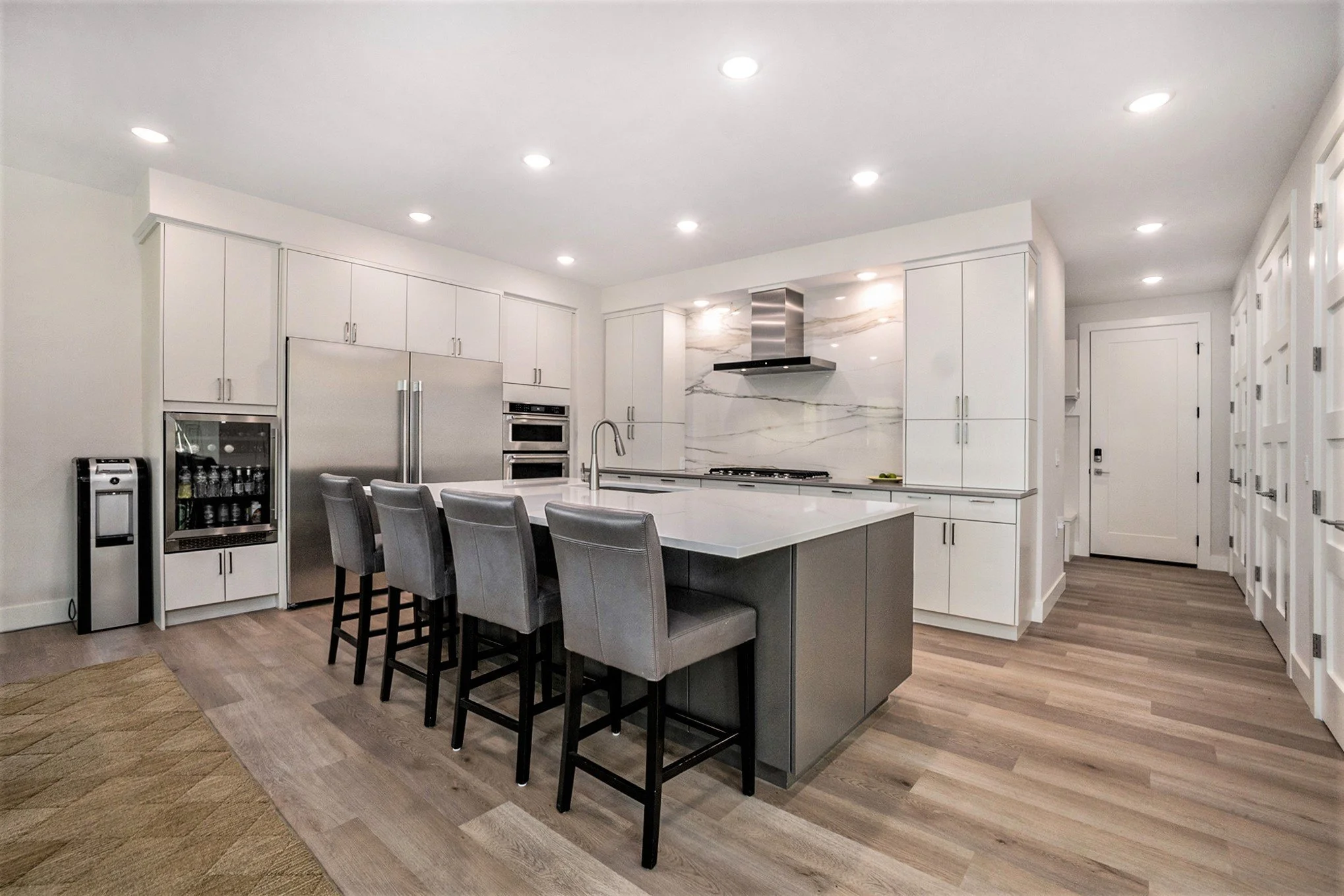 Modern kitchen with white cabinets, stainless steel appliances, a kitchen island with gray chairs, and a marble backsplash.