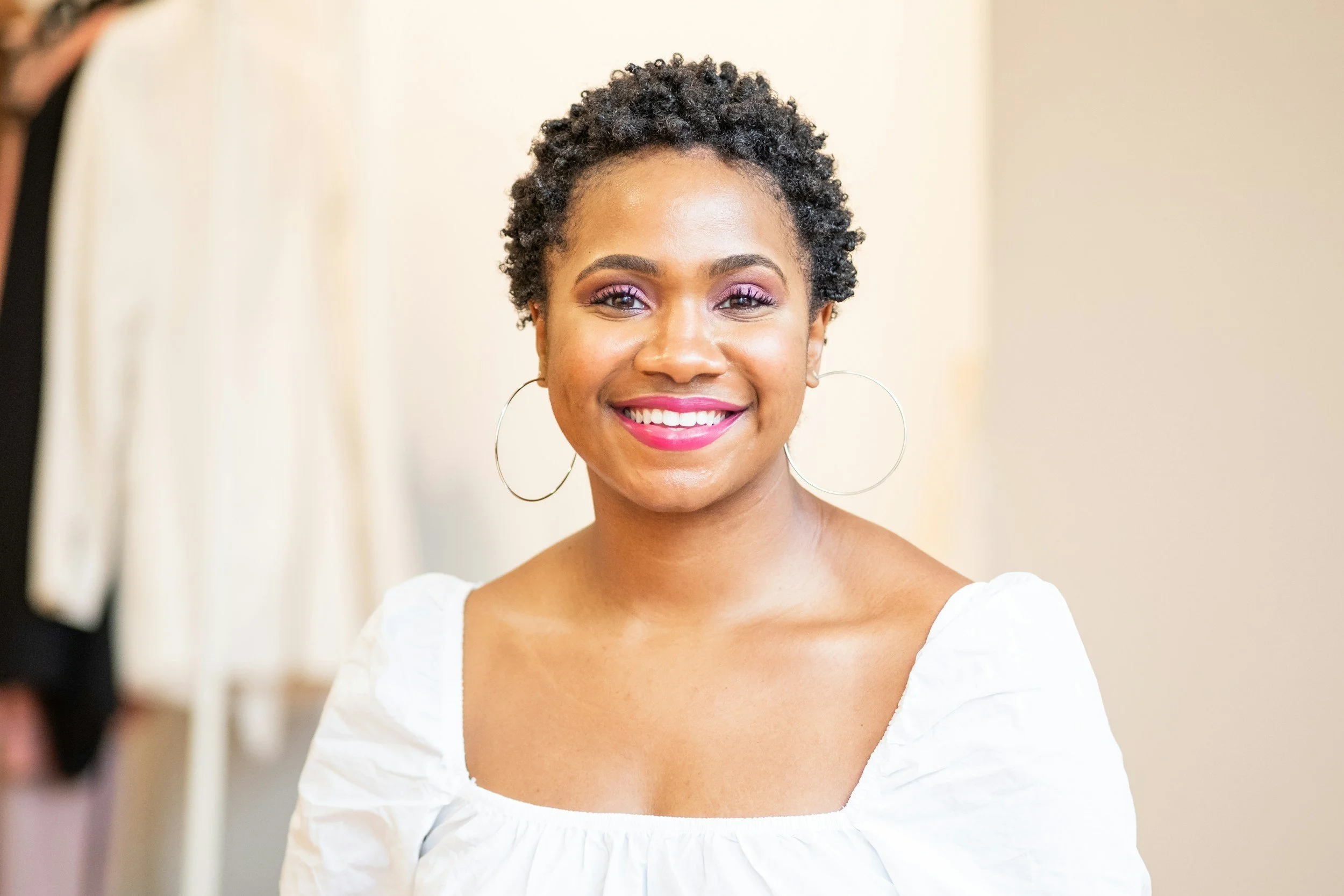 Woman with short curly hair, earrings, and white top smiling at the camera.
