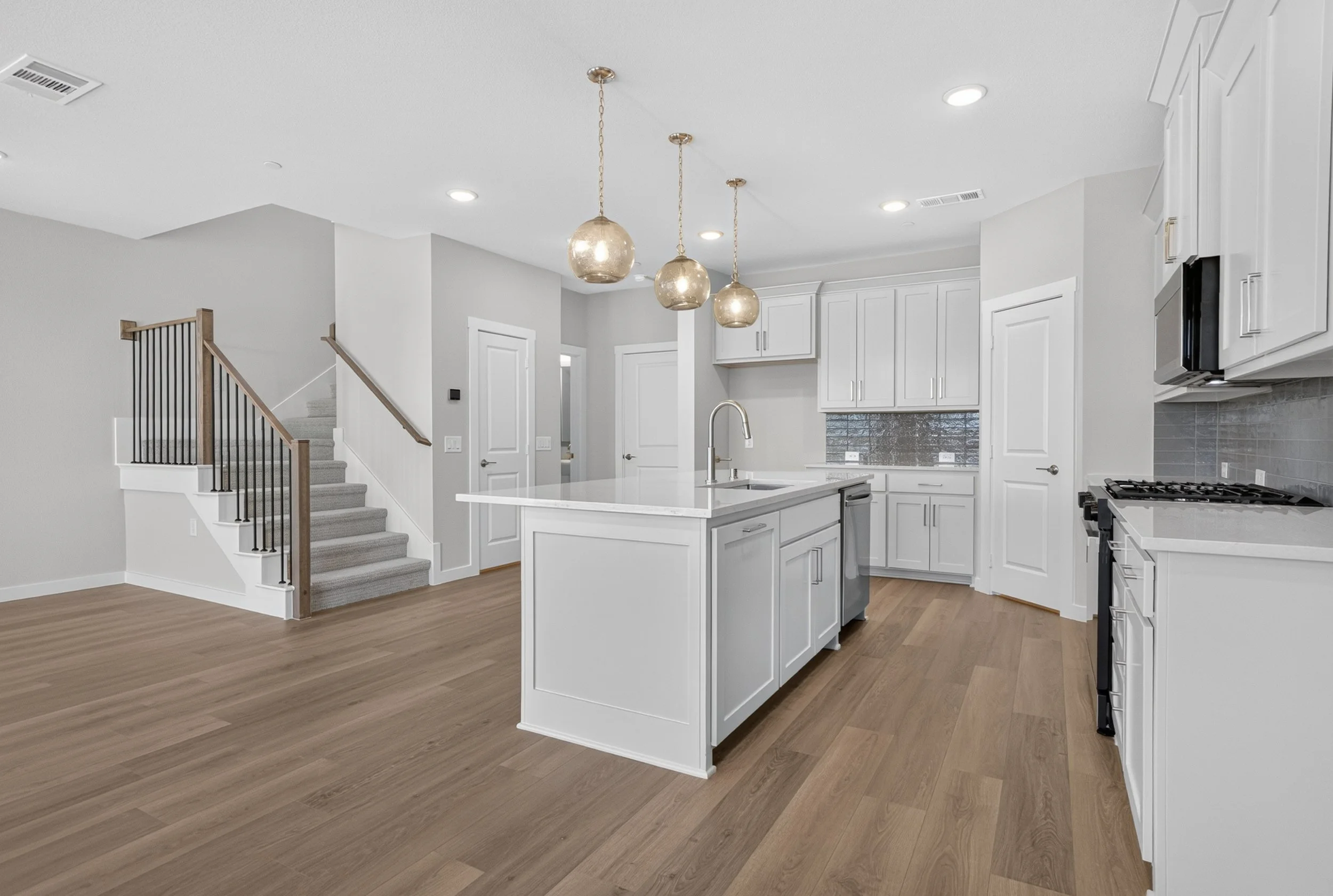 Modern kitchen with white cabinetry, a kitchen island, stainless steel appliances, pendant lights, and wood flooring.