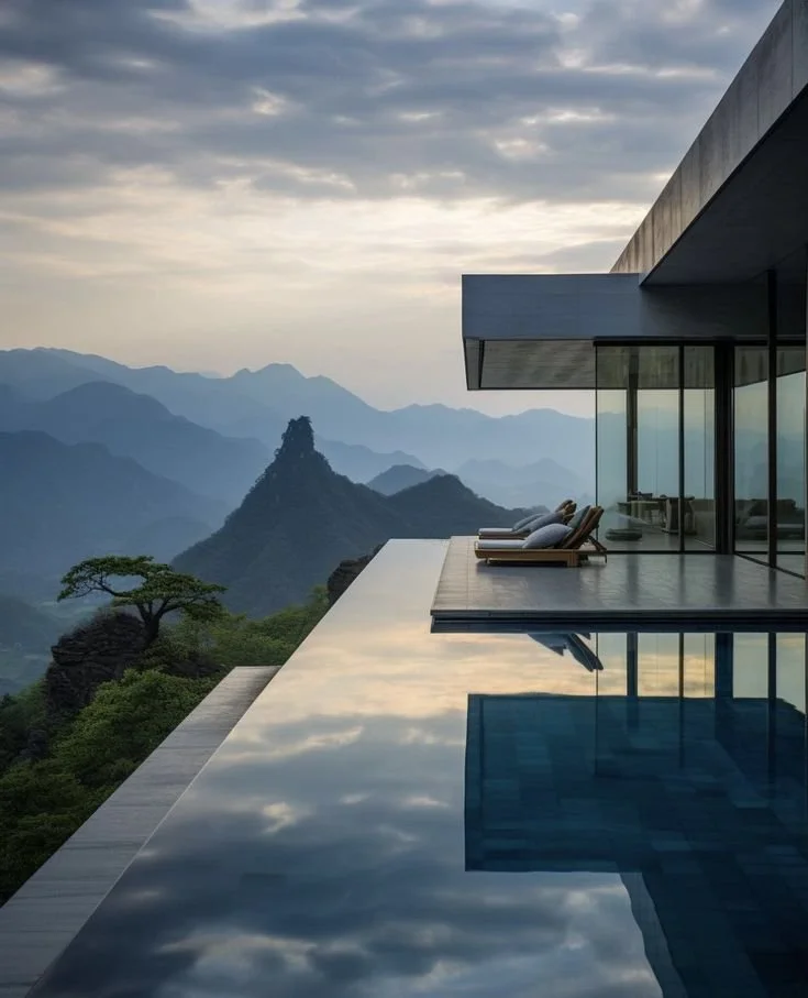 Modern house with outdoor infinity pool overlooking mountains and cloudy sky.