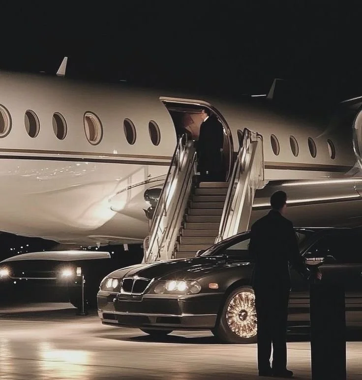 Man boarding a private jet via a staircase with a black luxury car parked nearby at night.