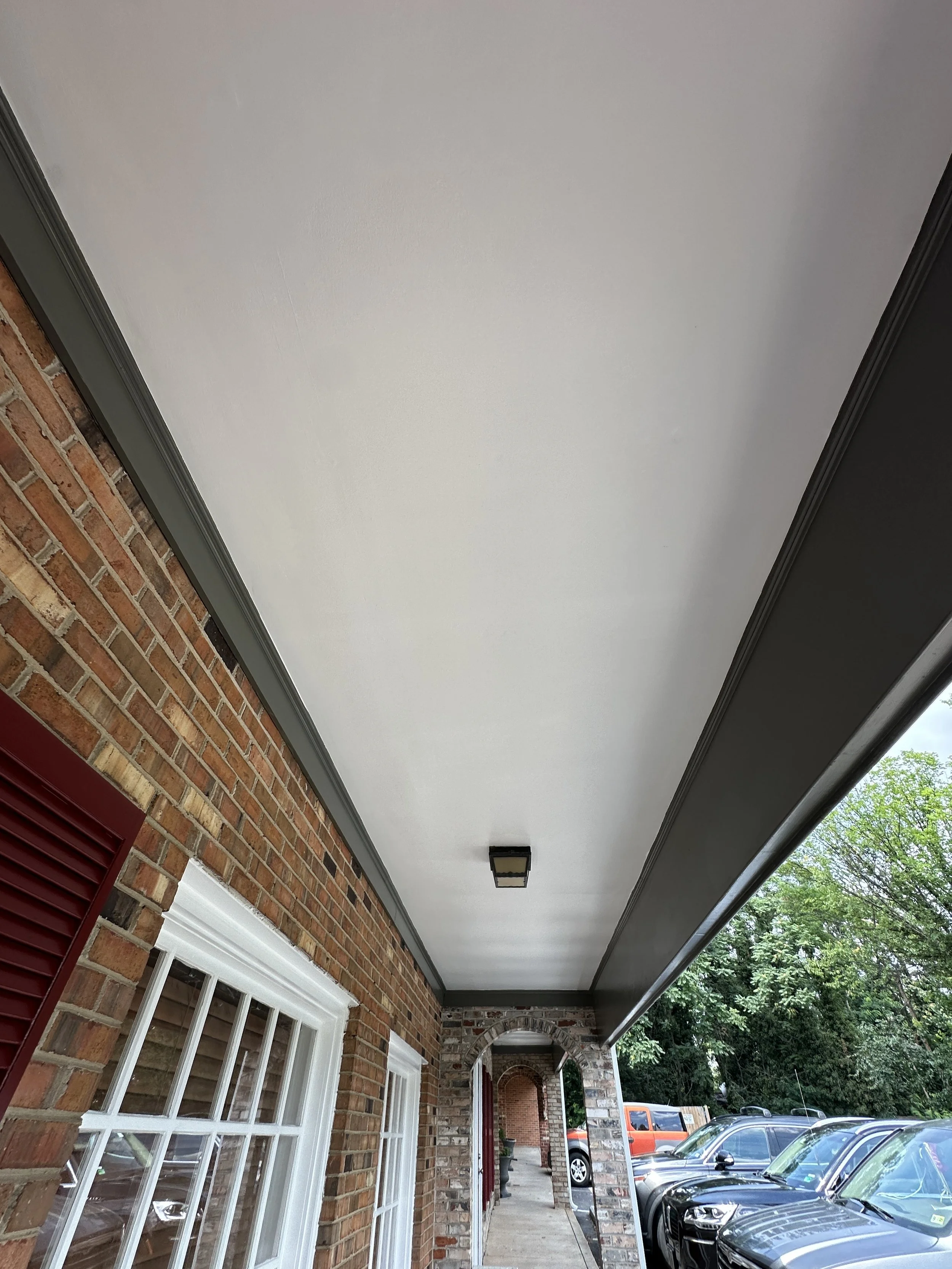 Overhead view of a porch with a white ceiling, brick walls, and parked cars to the side on a sunny day.