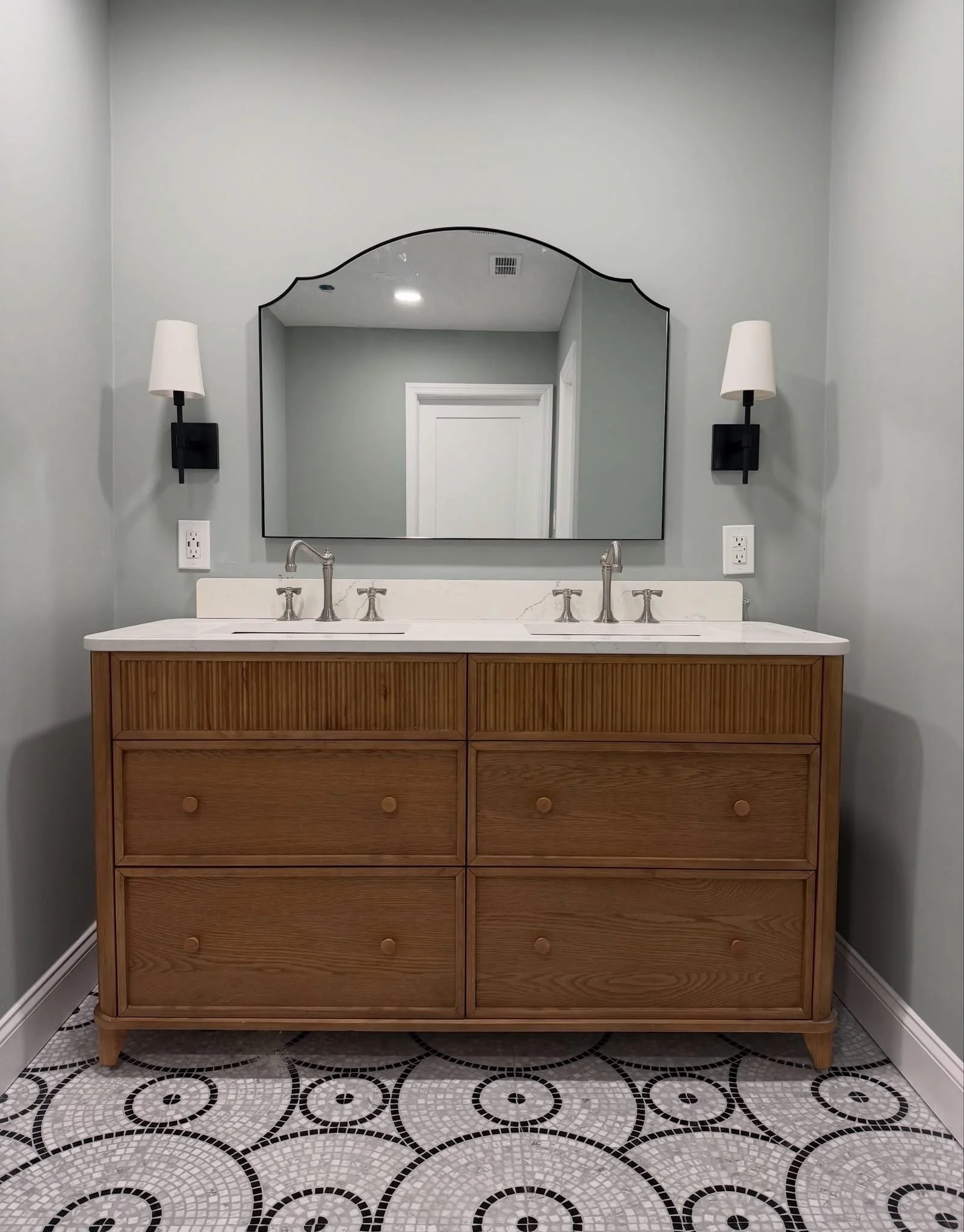 Bathroom with large mirror, double sink vanity with dark cabinets, bathtub, and windows with blinds, during renovation.