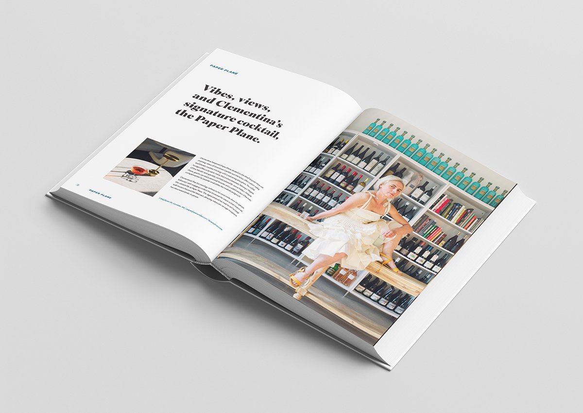 Open magazine showing an article about signature cocktails with a page featuring a woman sitting on a bench surrounded by bottles of alcohol and books.