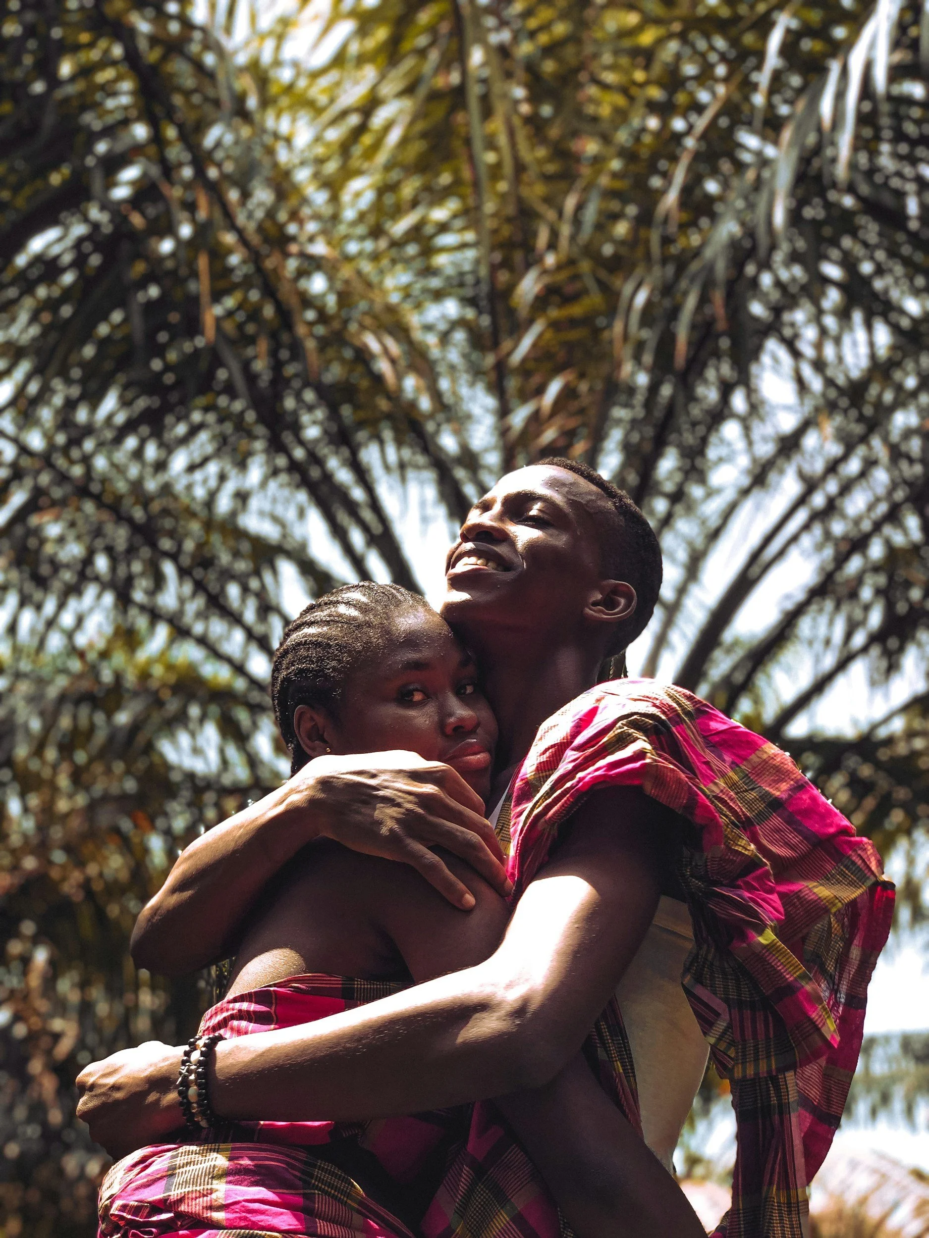 Two people embracing outdoors with palm fronds in the background.