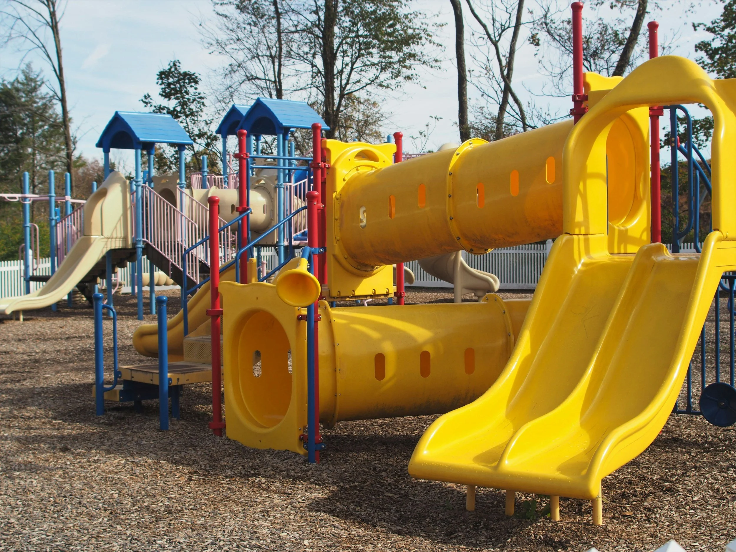 Colorful playground with multiple slides, tunnels, and climbing structures under a partly cloudy sky.