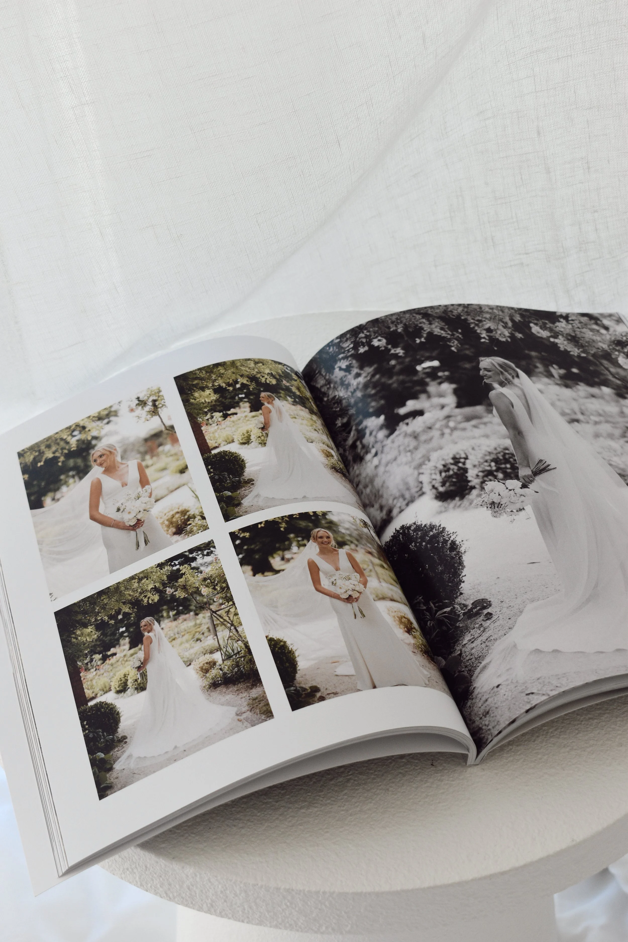 Open wedding photo album showing color and black-and-white images of a bride in a garden setting.