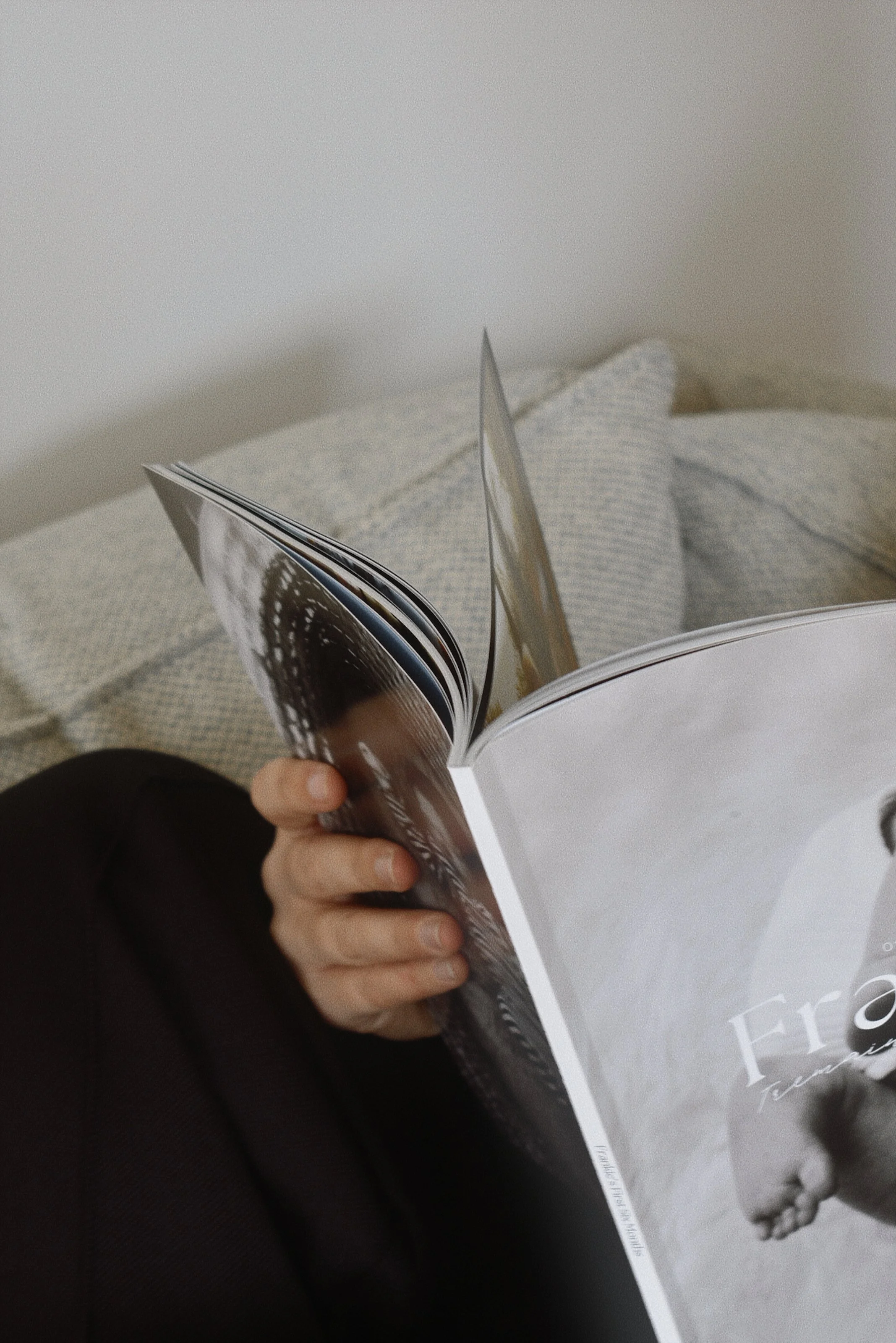 Person sitting on bed reading a magazine.