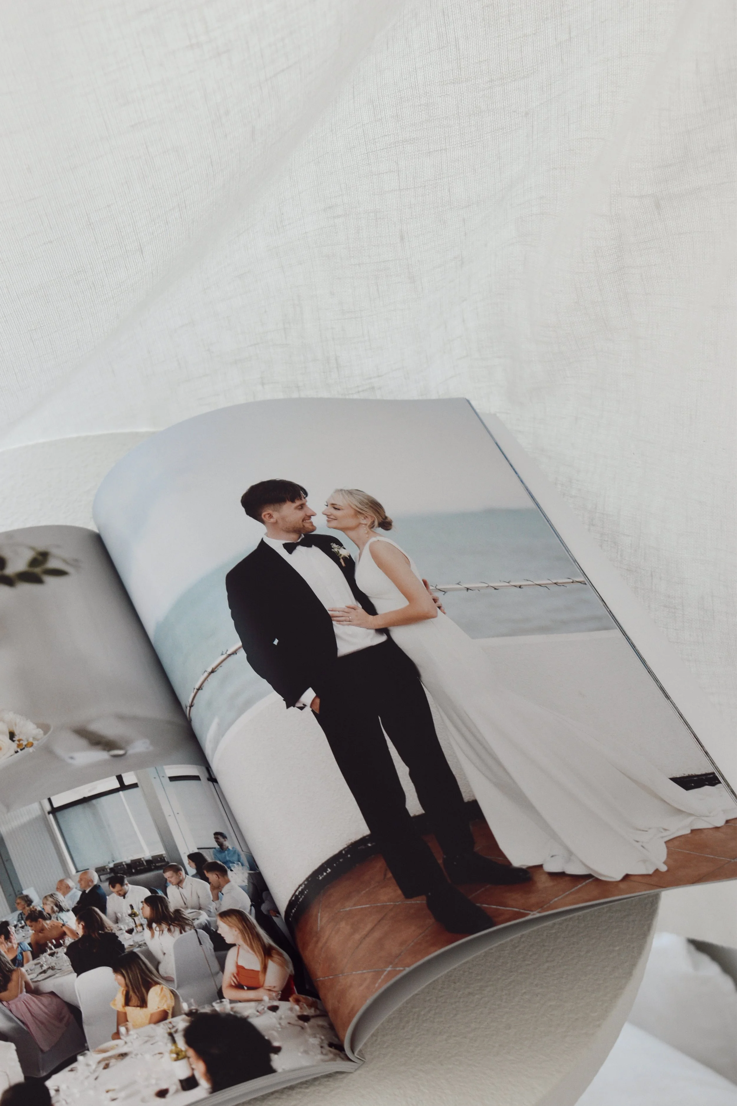 Open wedding photo album showing a bride and groom in wedding attire standing near the ocean on a boat.