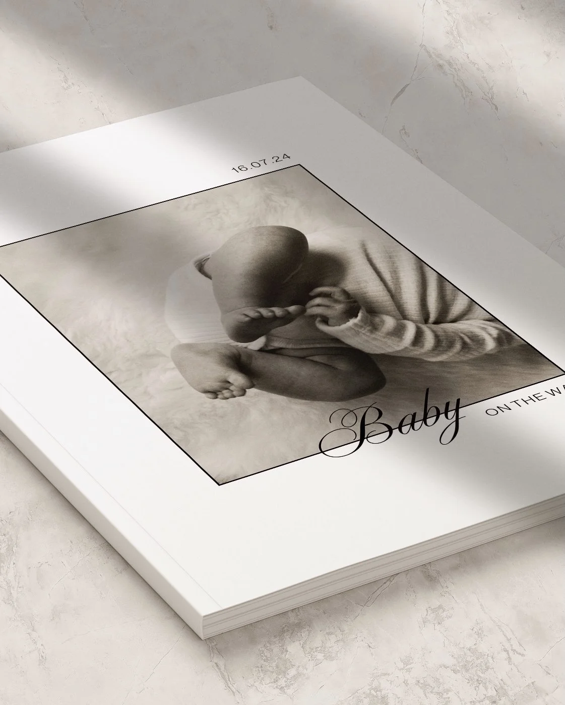 A white photo book with a black and white image of a baby in a fetal position on the cover, along with the text 'Baby on the W' and top date '16.07.24'.