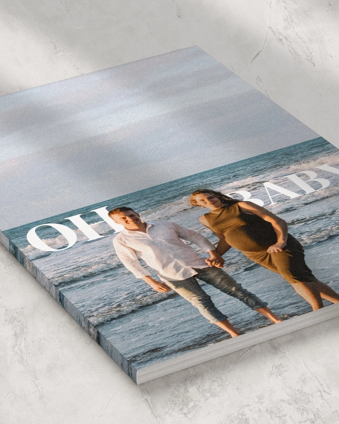 A magazine or photo book featuring a couple holding hands at the beach, with large white text reading 'ABOUT' across the image.