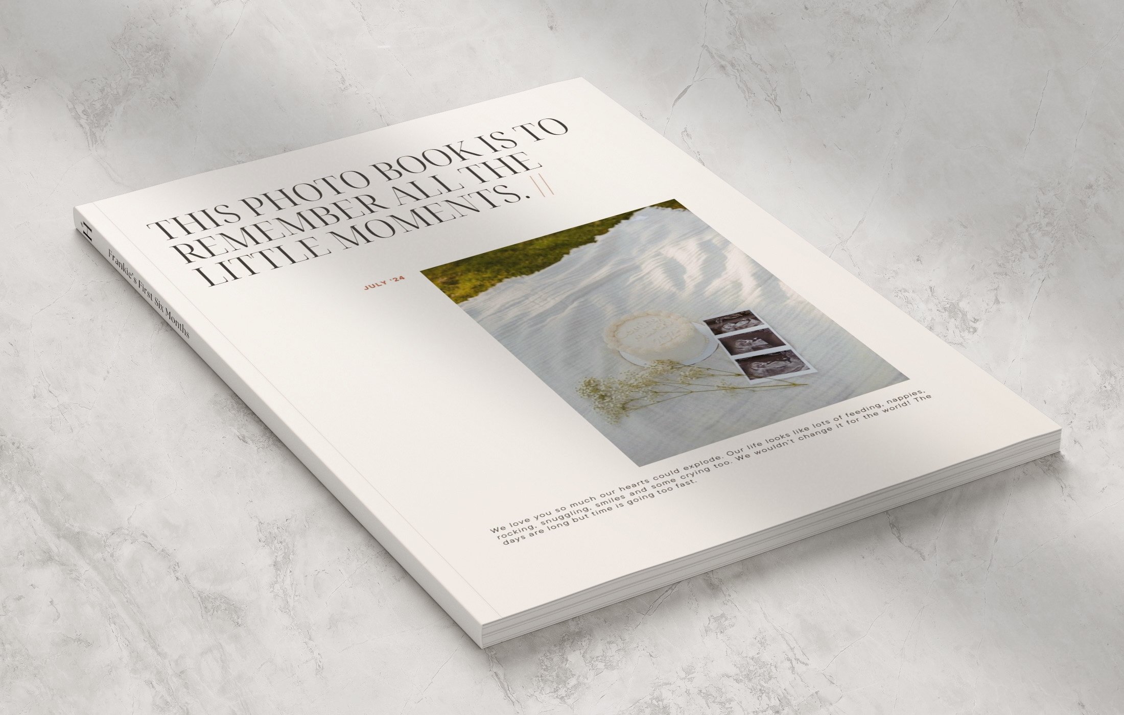 A white photo book titled "This photo book is to remember all the little moments." Open on a marble surface, displaying a page with a photo of a plate with a flower and three black-and-white images of a person, along with a paragraph of text.