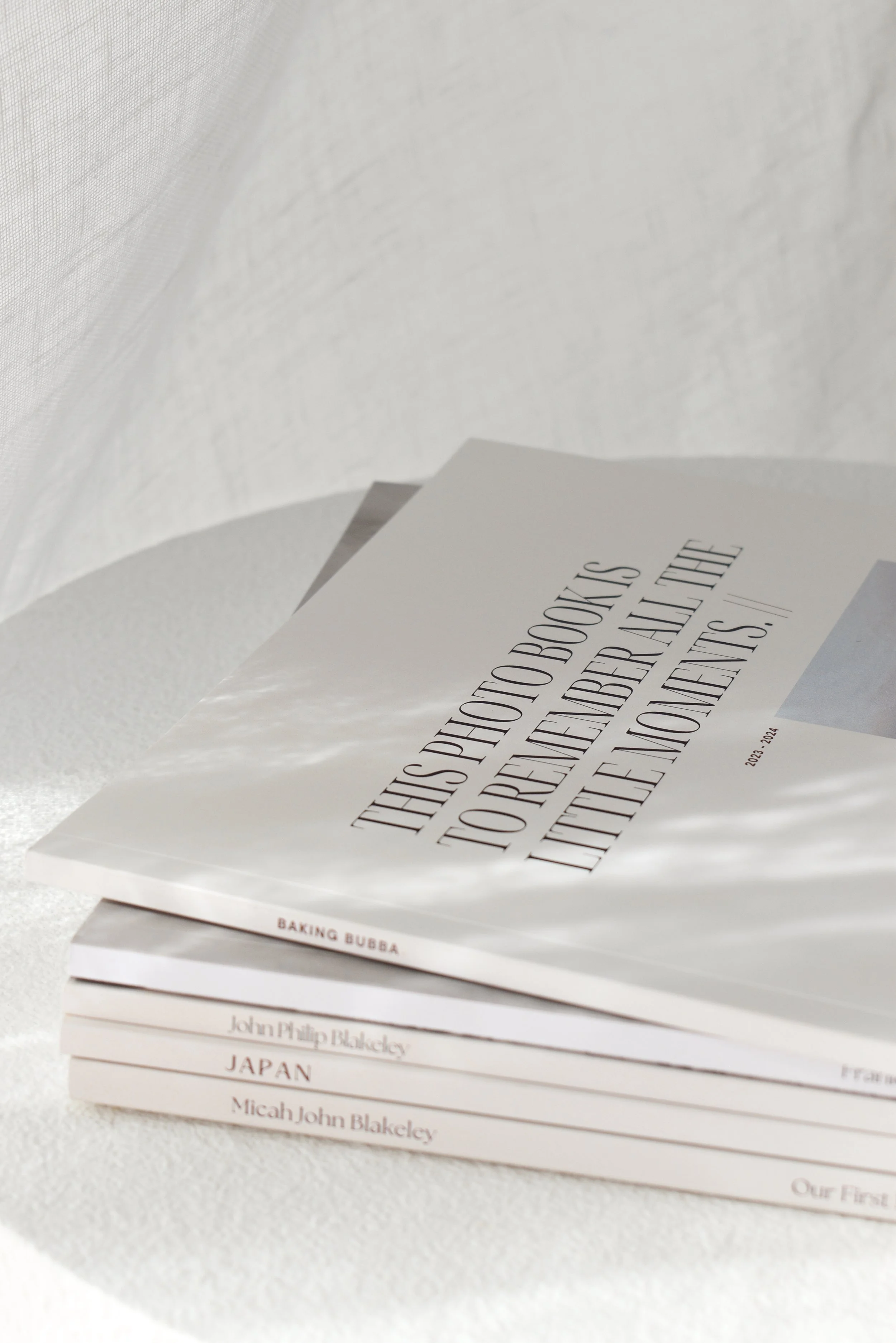 Stacked books with minimalist white covers on a textured white surface, with one book slightly open showing a cover with text about photo books.