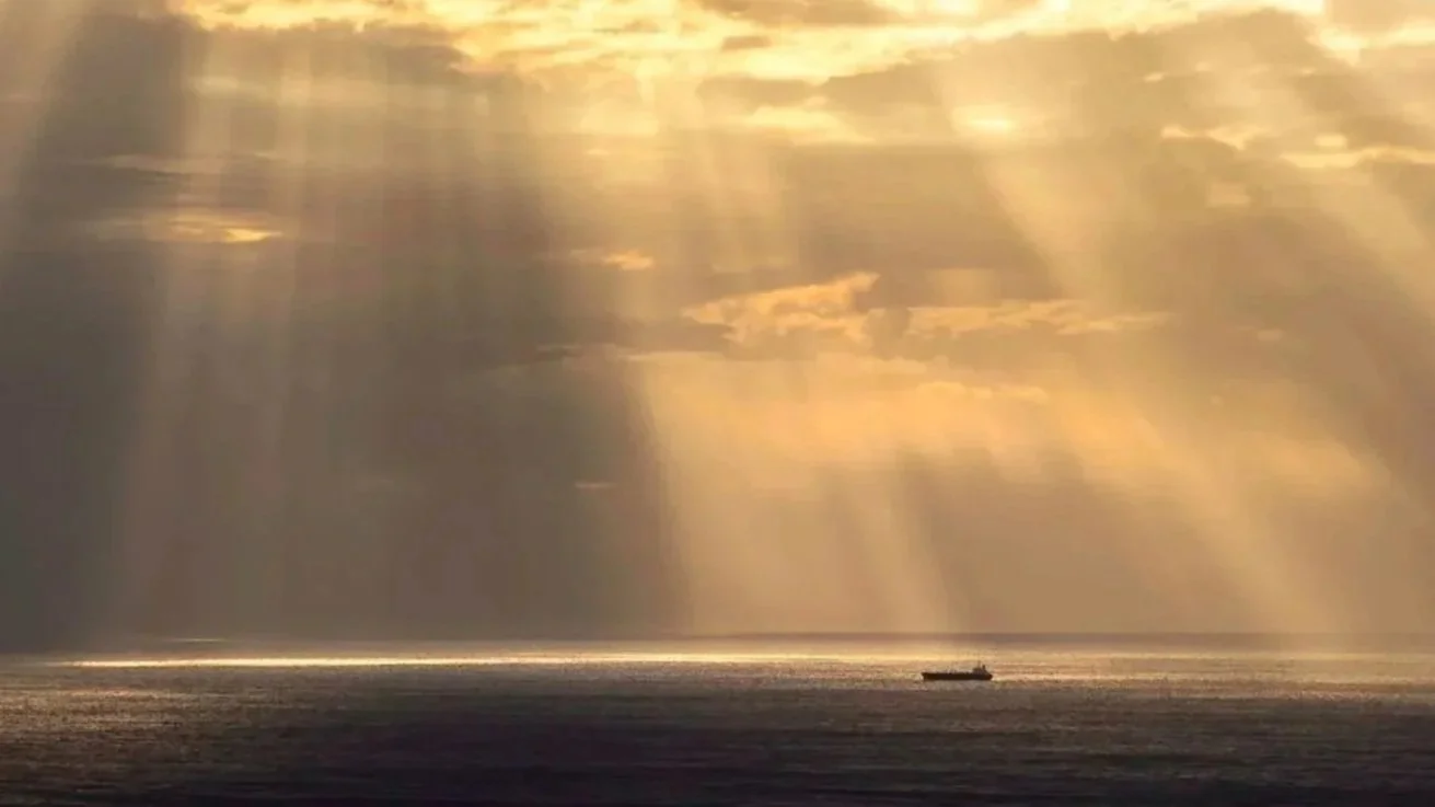 Sunlight breaking through clouds over the ocean, symbolizing clarity and guidance in actuarial decision-making.